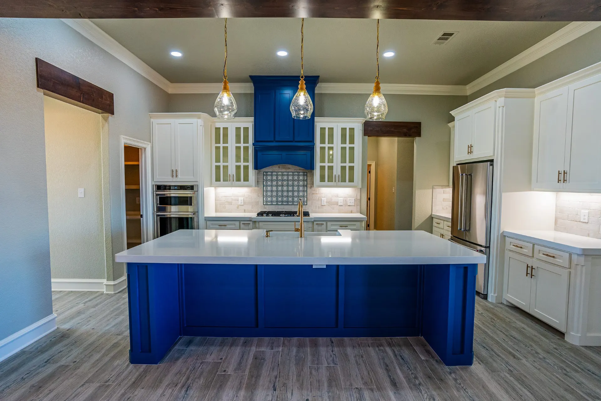 Wide view of the Eliam St Home kitchen with the cobalt blue island and arched hood, brass pendants and white glass-front perimeter cabinetry