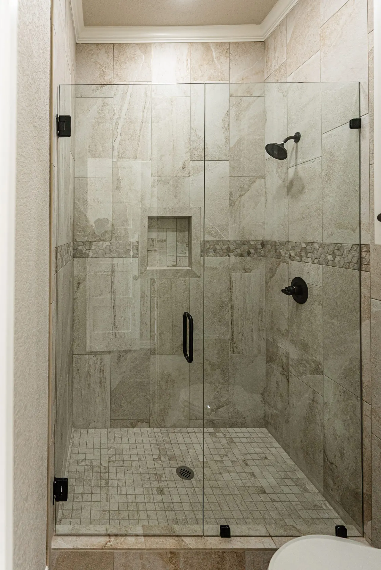 Walk-in shower at 1602 NW 12th St with beige marble-look tile, decorative mosaic band and matte-black fixtures