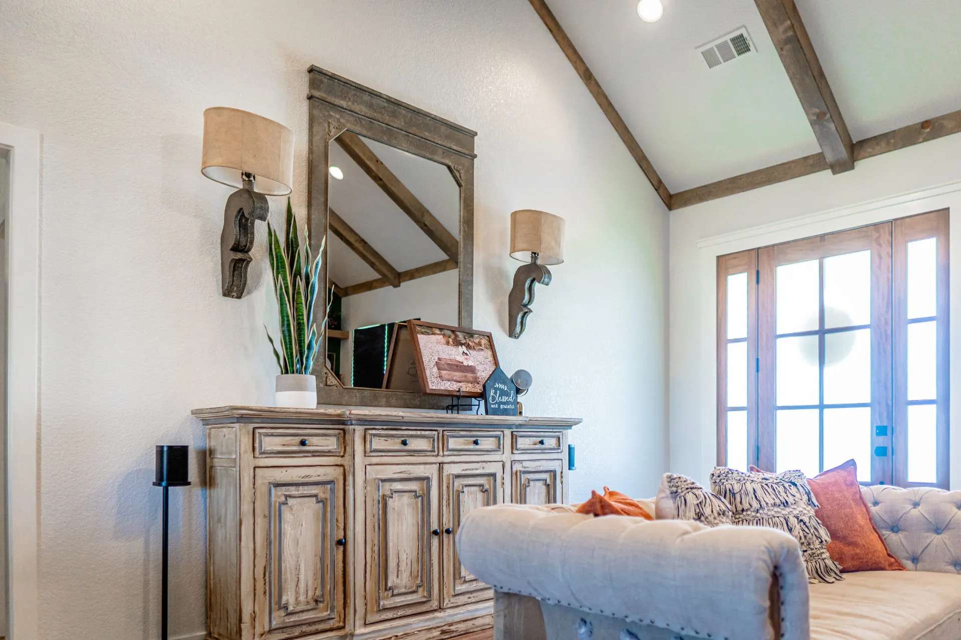 Living room vignette at the K Ave Farmhouse with a distressed sideboard, carved wall sconces, a large distressed mirror and candlestick lamps
