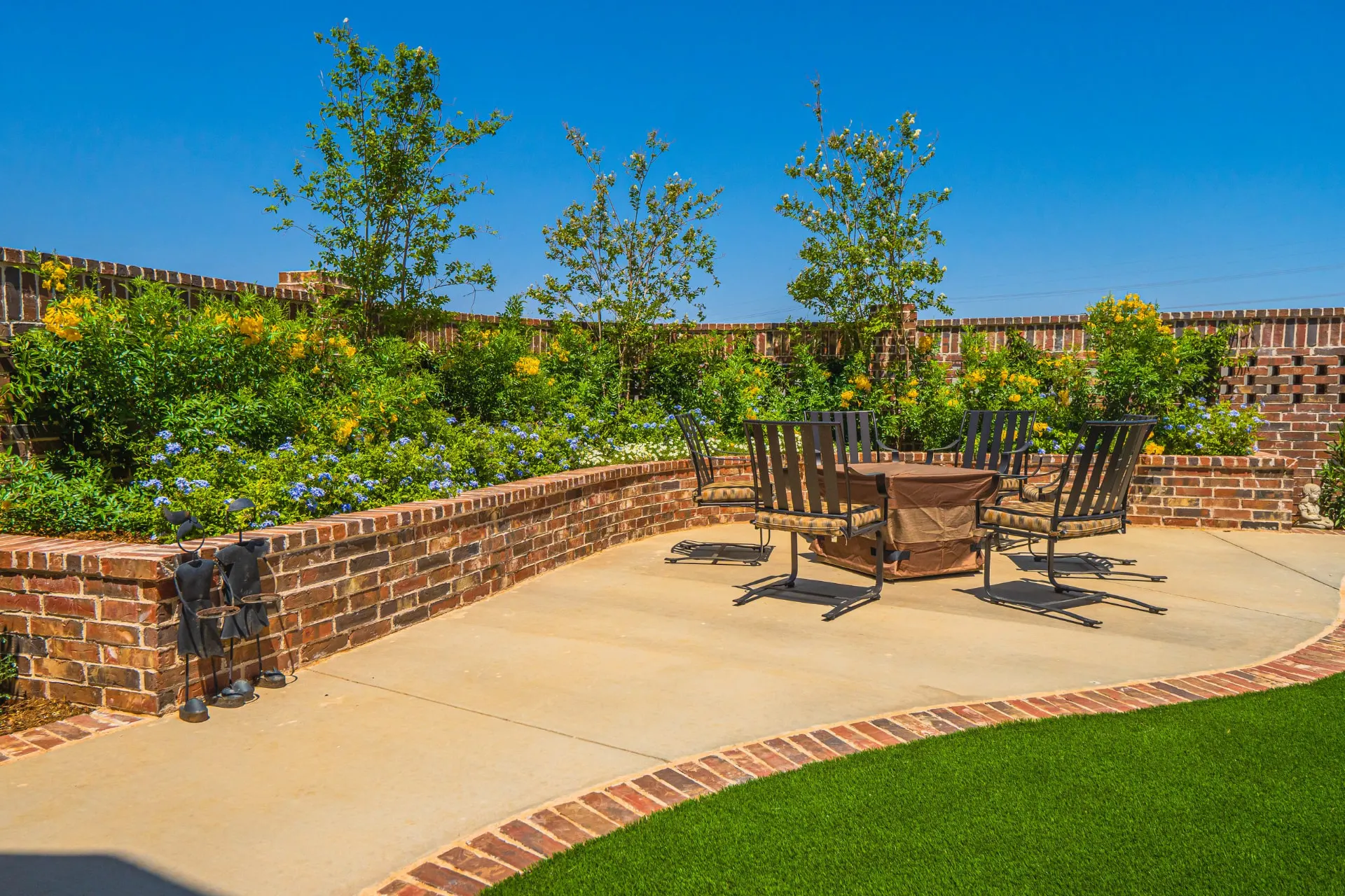 Backyard fire-pit patio at the Wraparound Porch Home enclosed by curved brick planters full of yellow and blue blooms