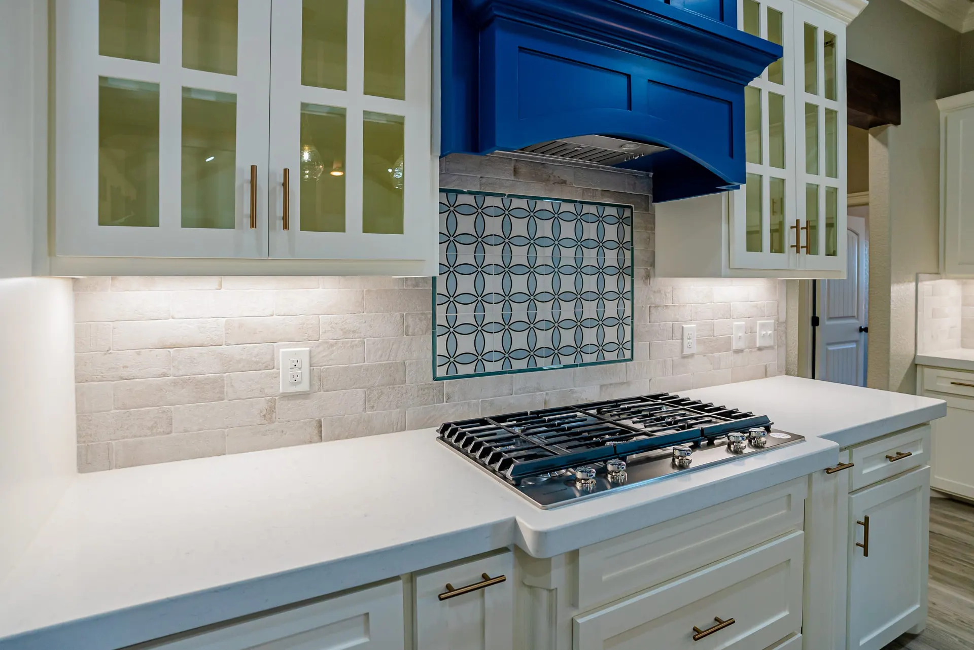 Detail of the Eliam St Home cooktop under the cobalt arched hood with the quatrefoil tile backsplash and brass hardware