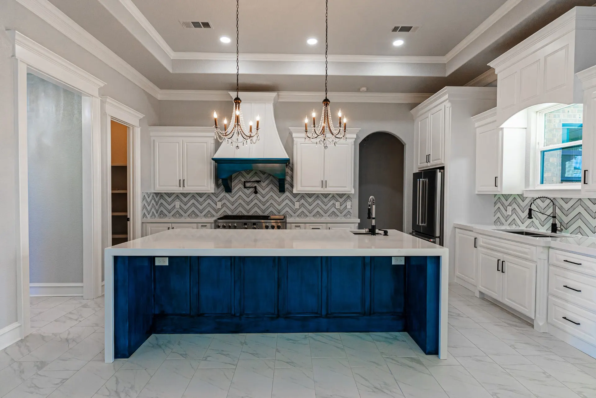 Kitchen island at 1511 NW 12th St in hand-rubbed blue beneath twin crystal chandeliers with a white panel vent hood