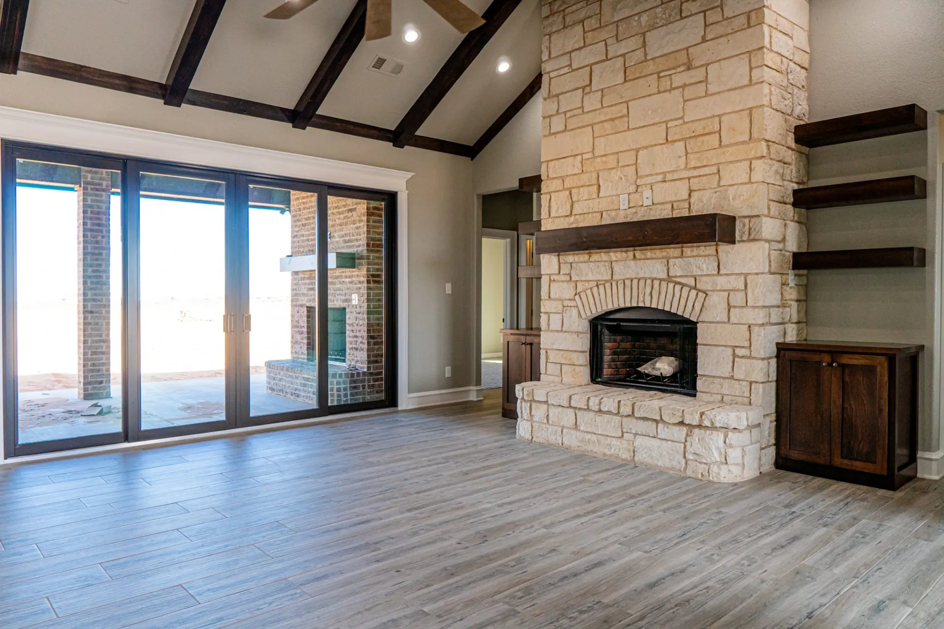 Great room at the 12th St Home with a vaulted ceiling and dark wood beams over a full-height cream stone fireplace with a dark timber mantel