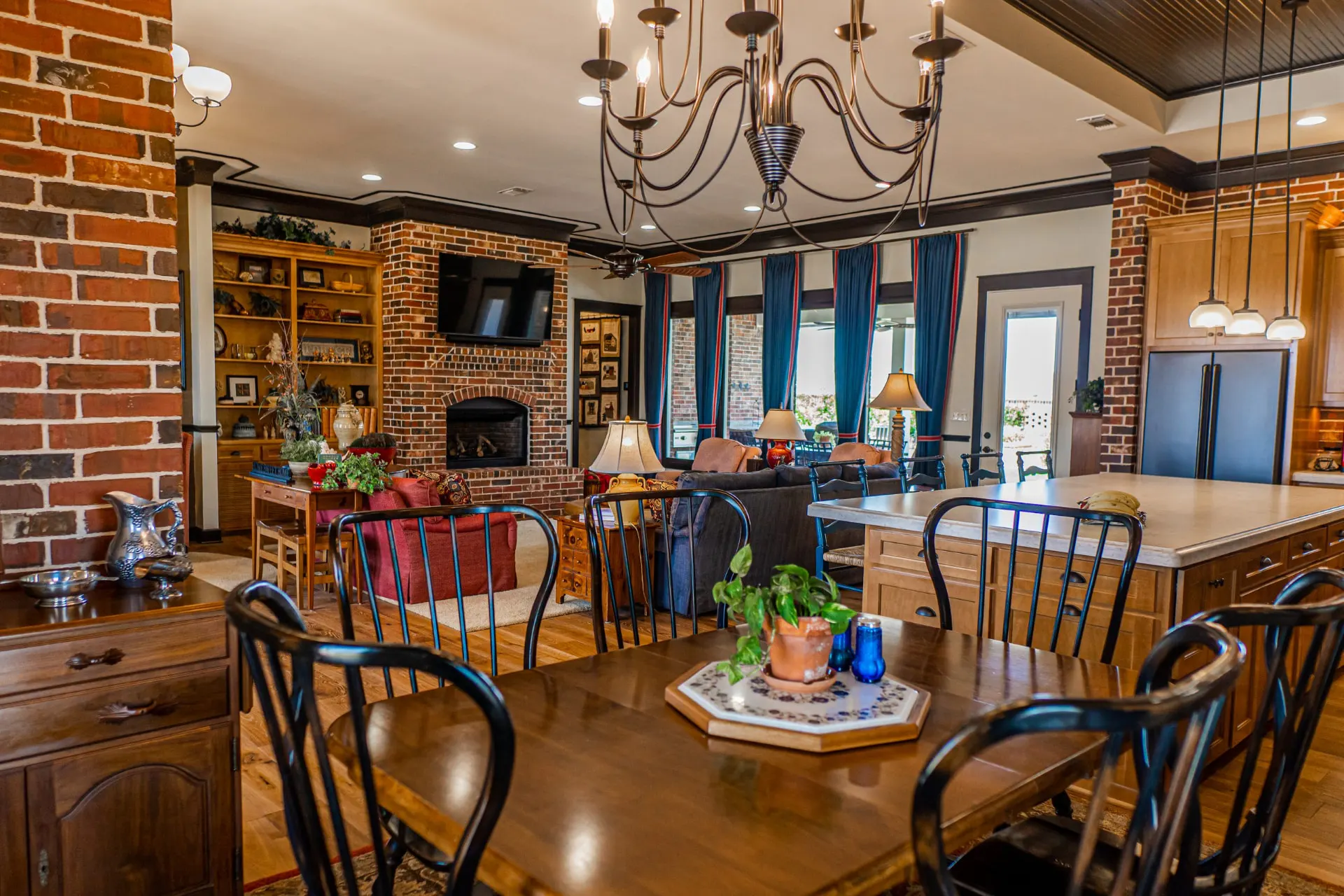 View from the dining table at the Wraparound Porch Home across the open living room to a red brick fireplace and the kitchen island
