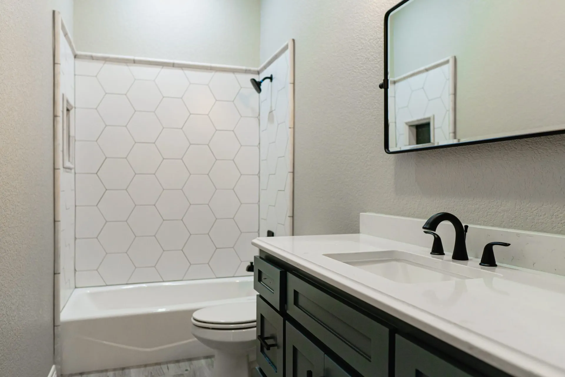 Bathroom at the 12th St Home with a dark green vanity, white quartz top, black fixtures and a white hexagon-tile tub and shower surround