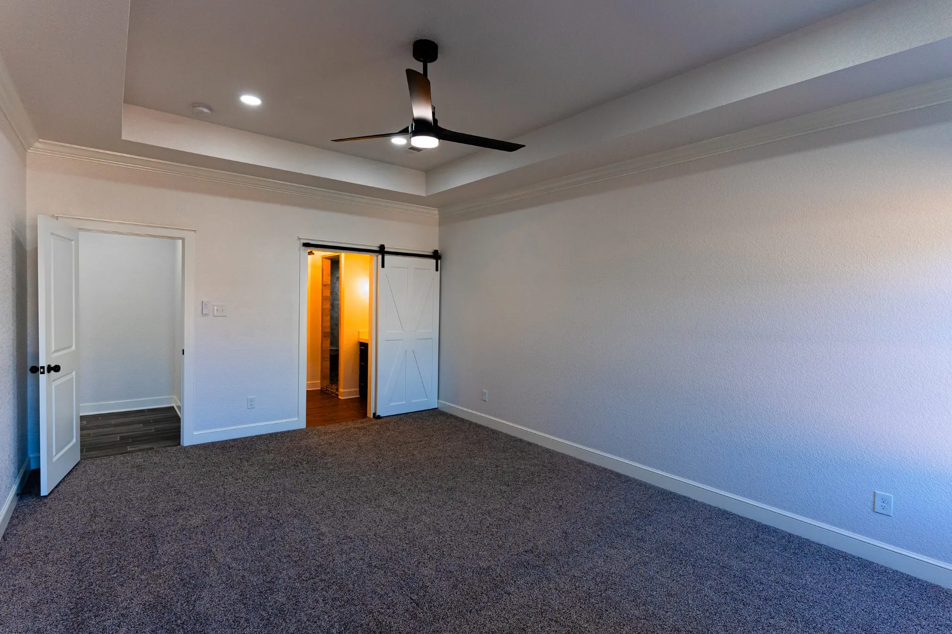 Same bedroom at 718 K Ave from the opposite angle, with a white sliding barn door on black hardware to the ensuite
