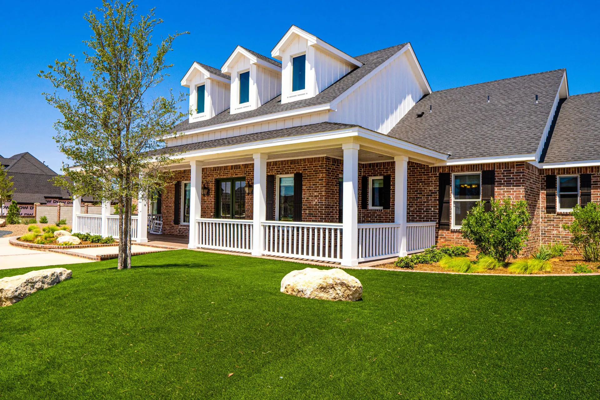 Corner of the wraparound porch at the Wraparound Porch Home with tapered white columns, railings and young trees in the new landscaping