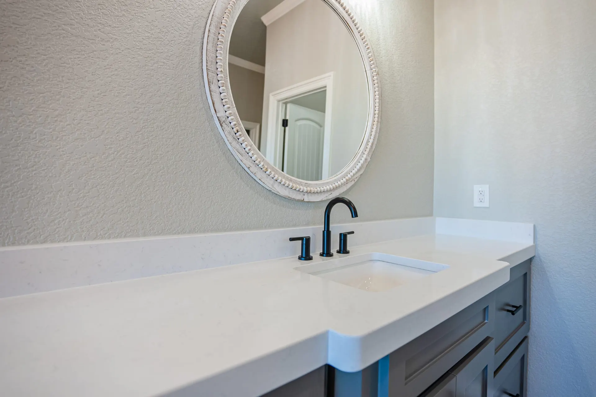 Close-up of the Eliam St Home bath vanity with a black faucet, white quartz top and a distressed white round mirror