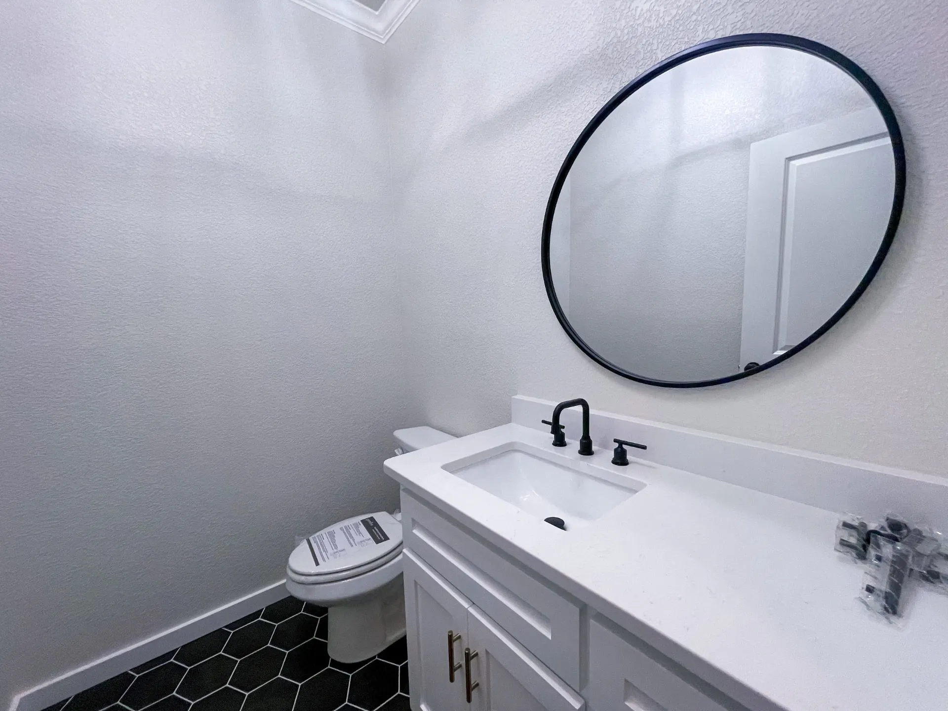 Powder room at 1615 NW 12th St with round black-framed mirror, matte-black faucet, white vanity and black hexagon floor tile