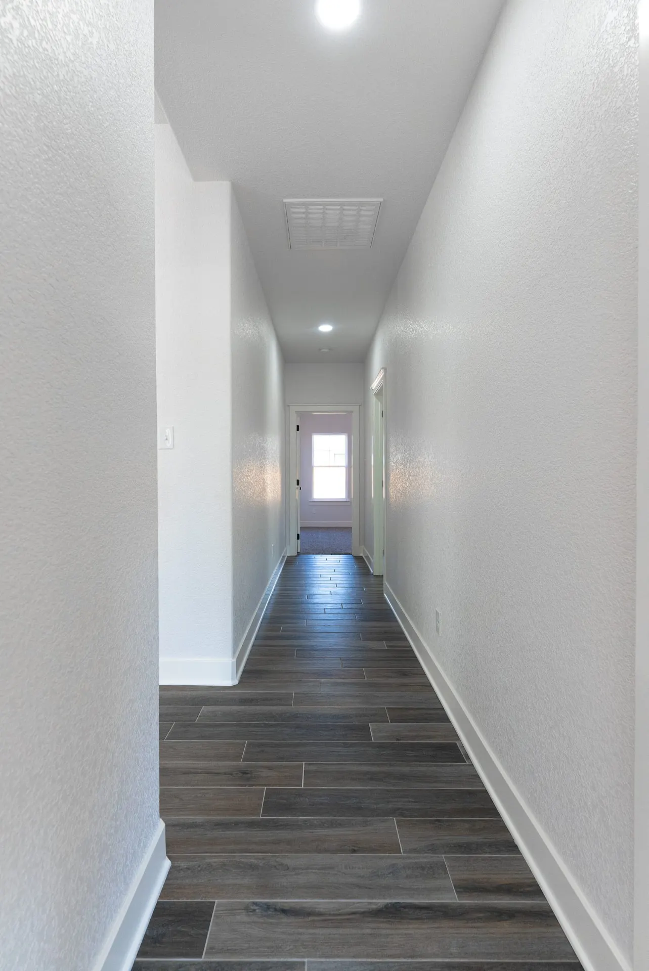 Long hallway at 718 K Ave with dark wood-look floors and recessed lights opening to a sunlit bedroom