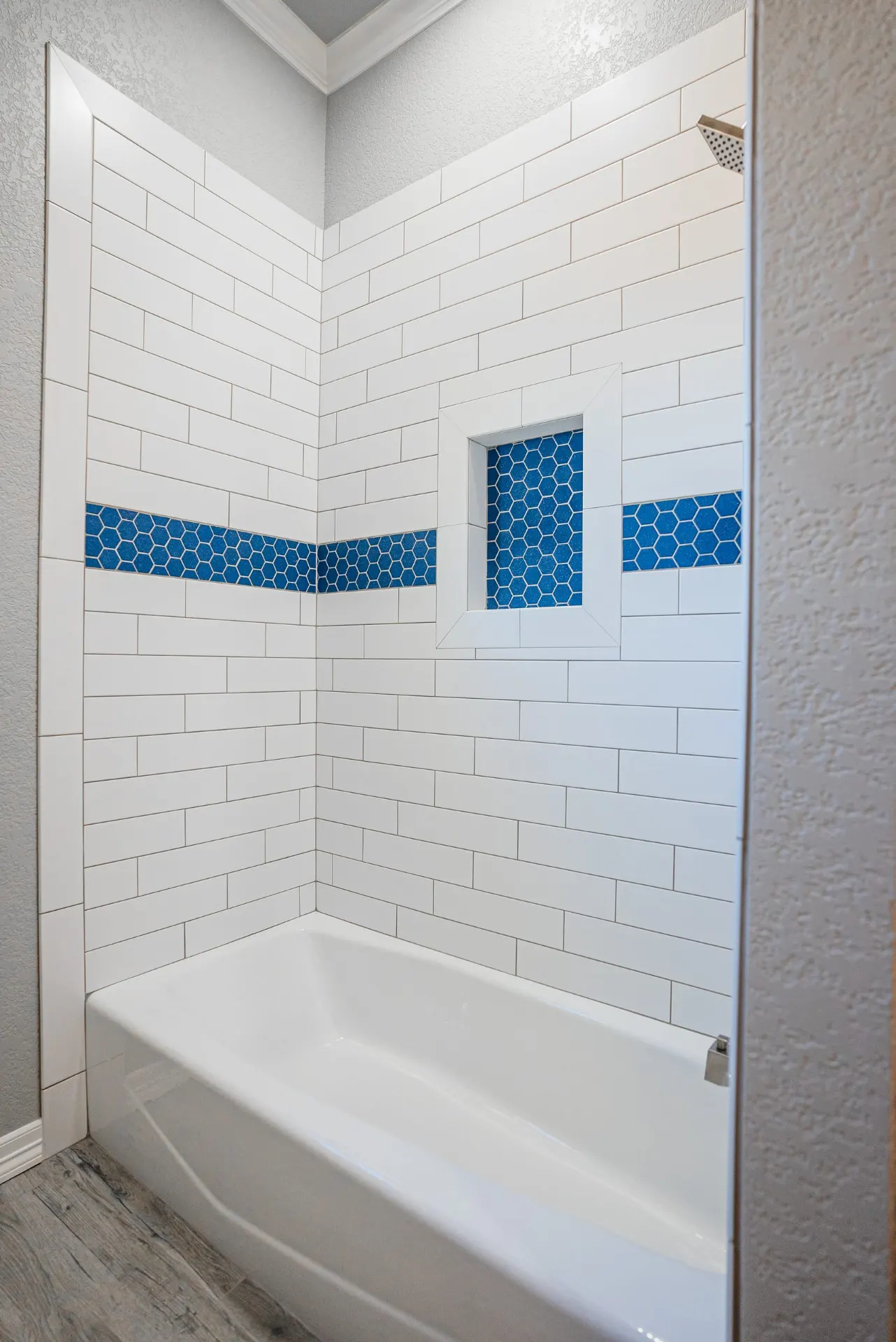 Tub shower at the Eliam St Home with white subway tile, a cobalt blue hexagon mosaic band and matching framed niche over the tub