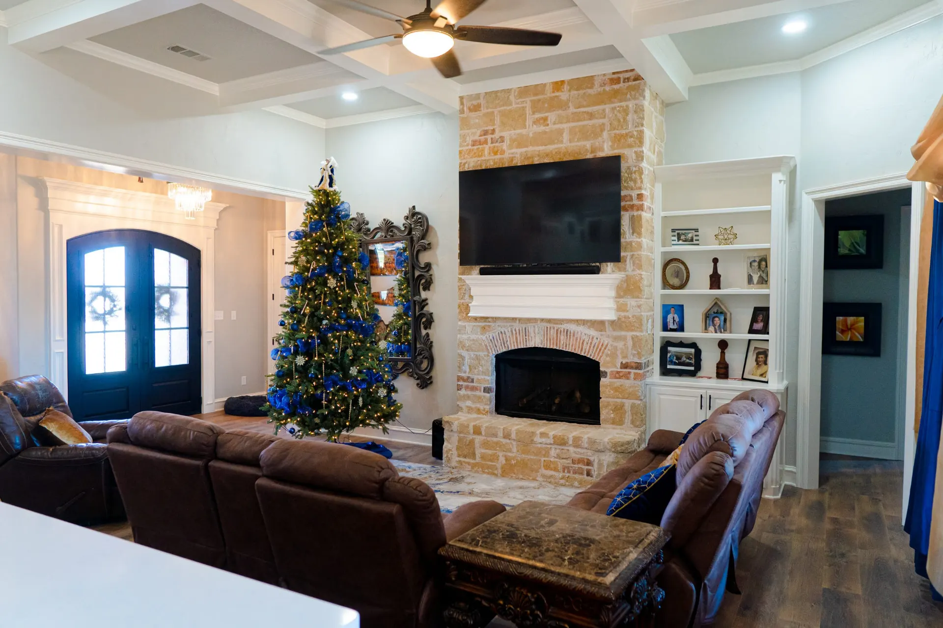Great room at 8821 Shawn Dr looking toward the arched iron entry doors, with a stone fireplace, white built-ins and a coffered ceiling
