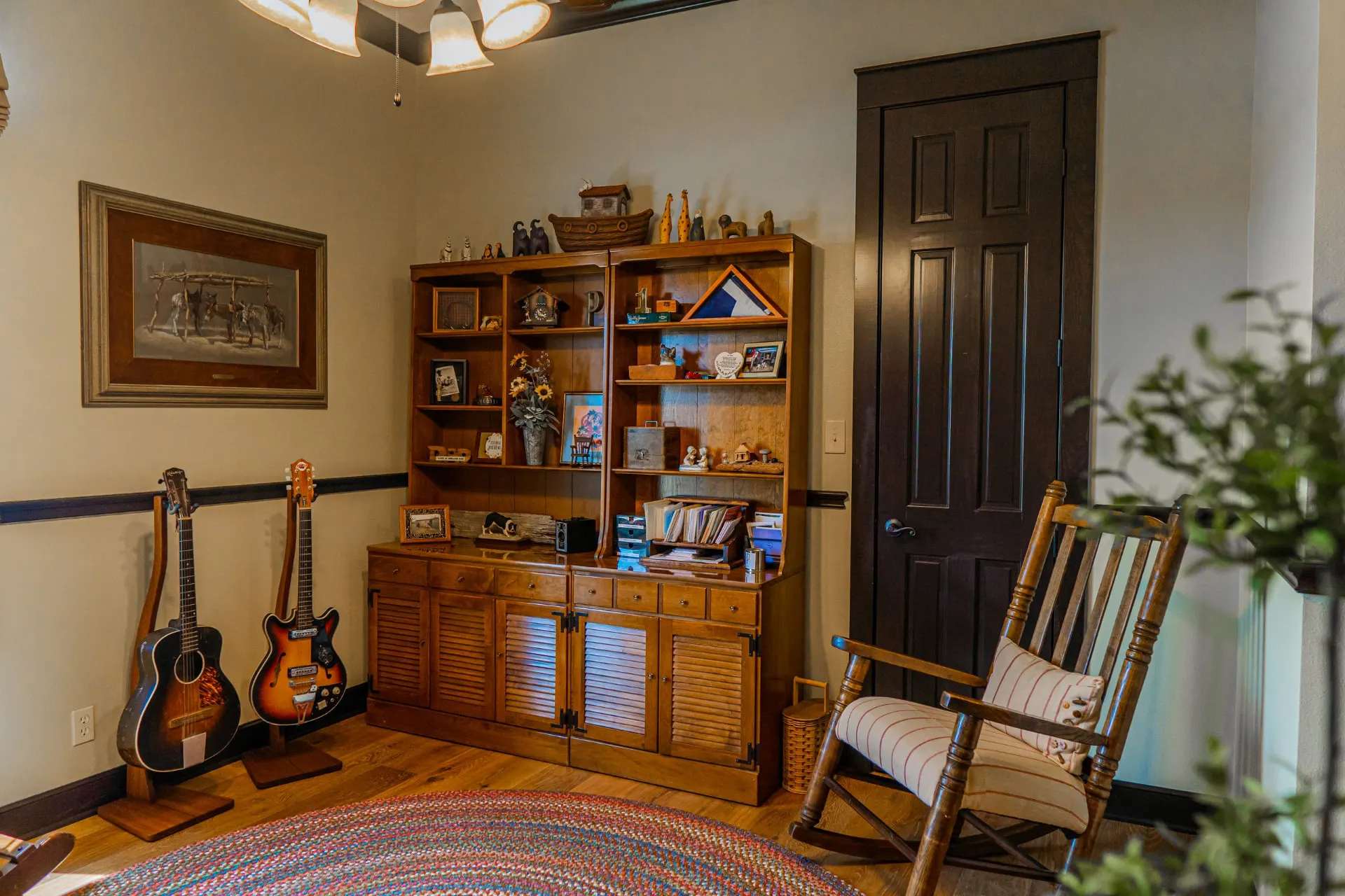 Music corner at the Wraparound Porch Home with two guitars on stands, an antique hutch and a rocking chair beside a dark paneled door
