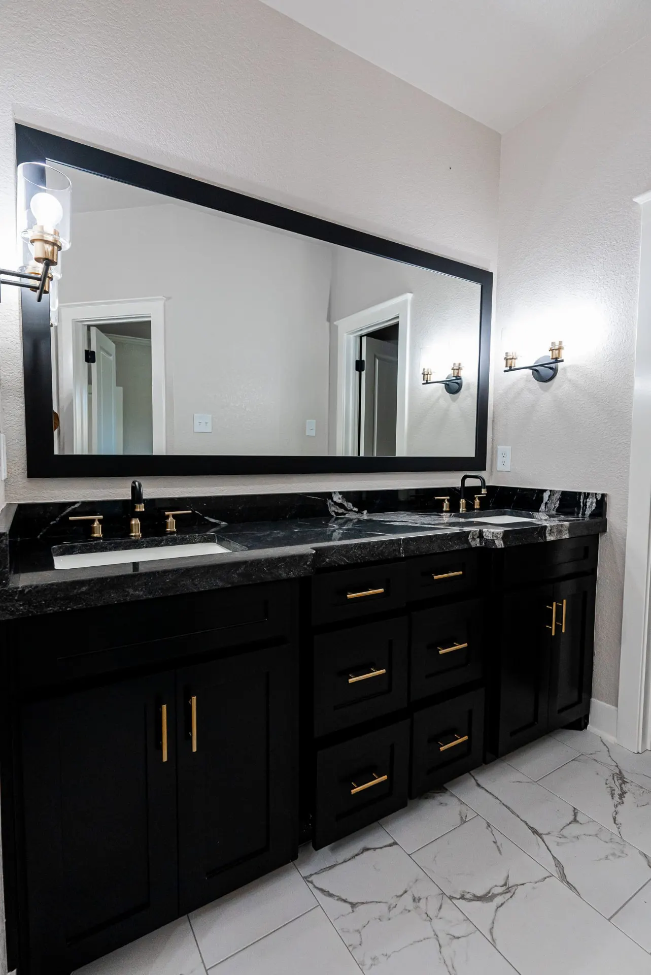 Primary double vanity at 708 K Ave with black cabinetry, black marble counters, brushed gold faucets and a wide black-framed mirror