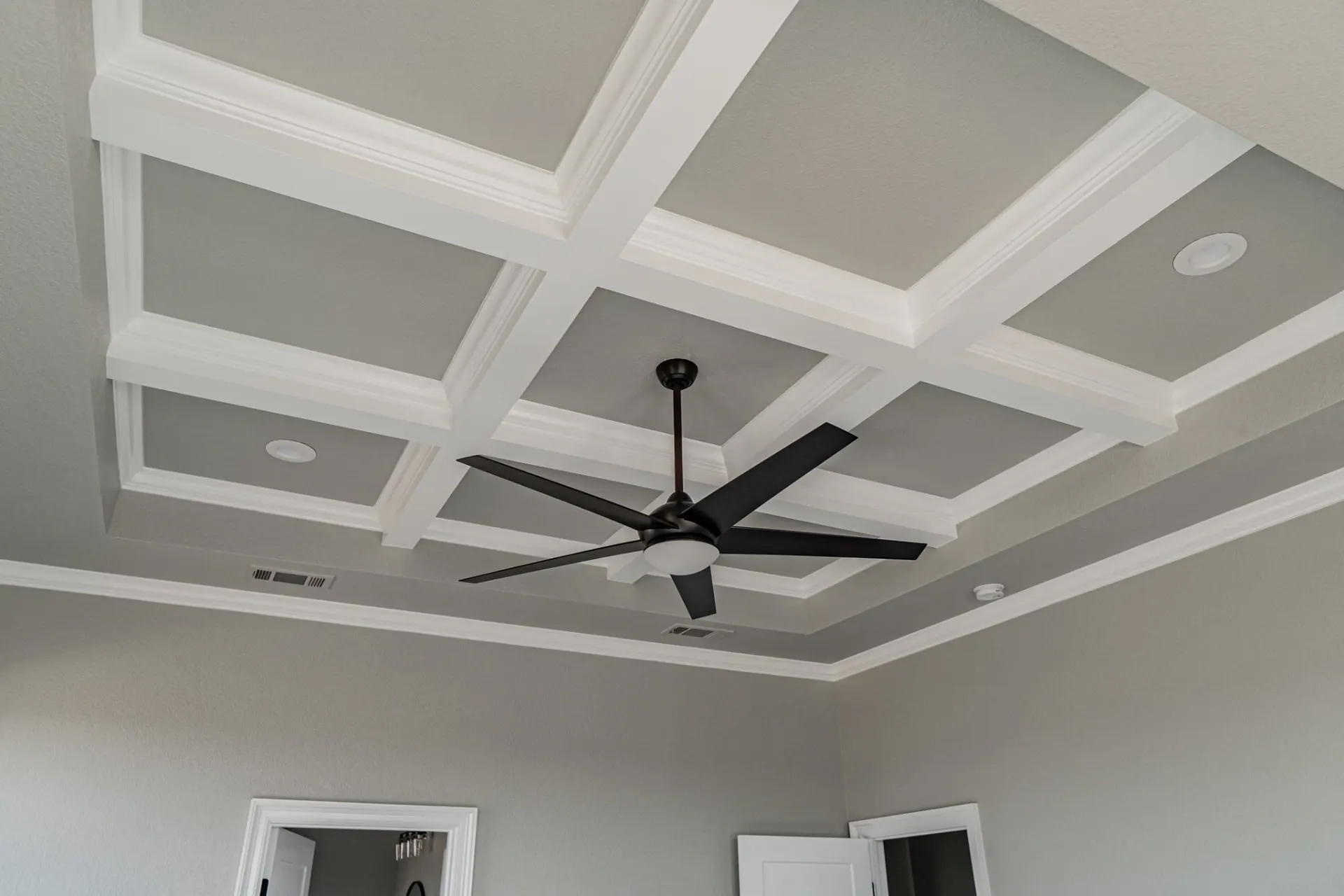 Coffered tray ceiling detail in the 12th St Home primary bedroom with a five-blade dark fan