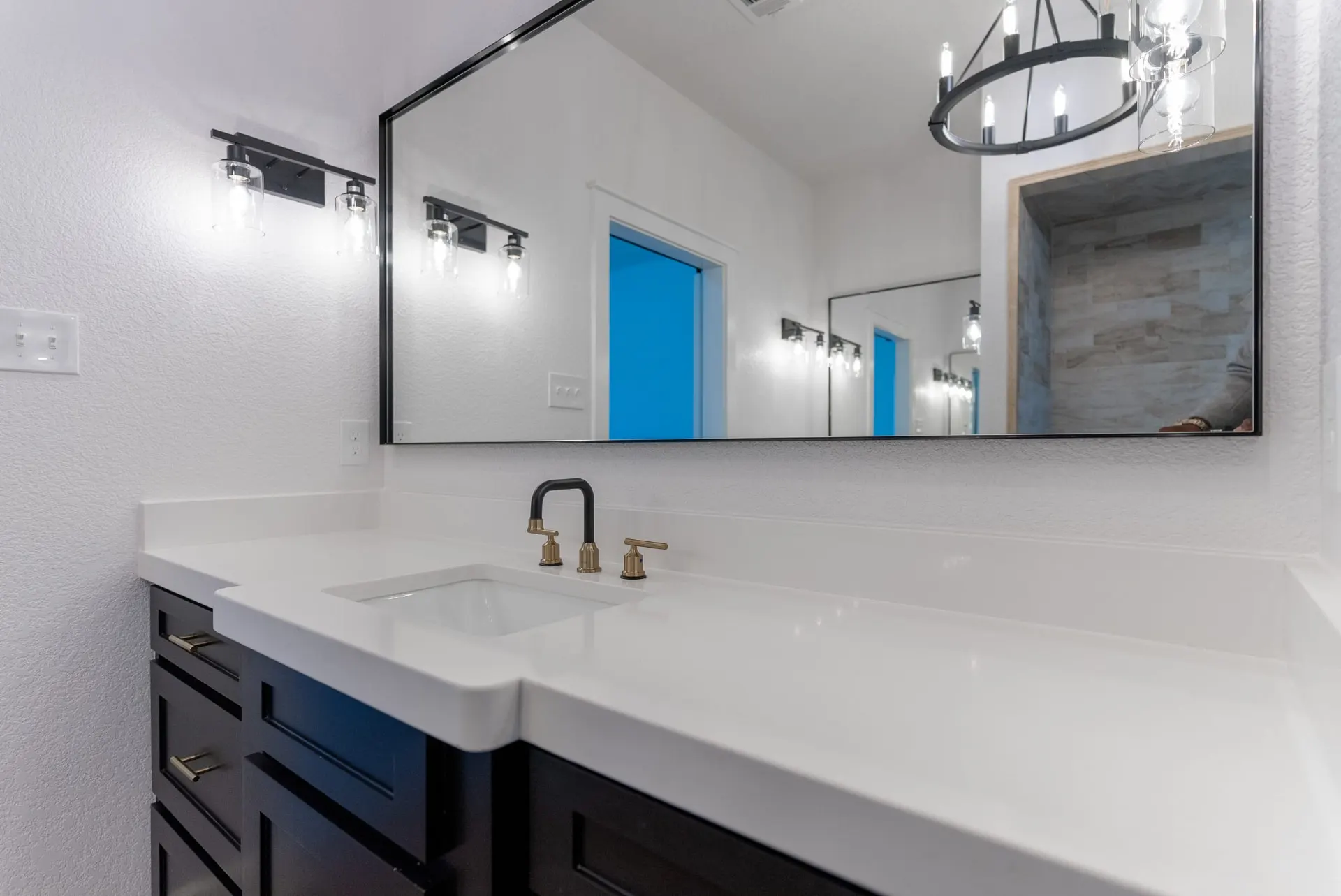 Vanity at 718 K Ave with dark shaker cabinets, a white countertop, black-framed mirror and black-and-gold fixtures