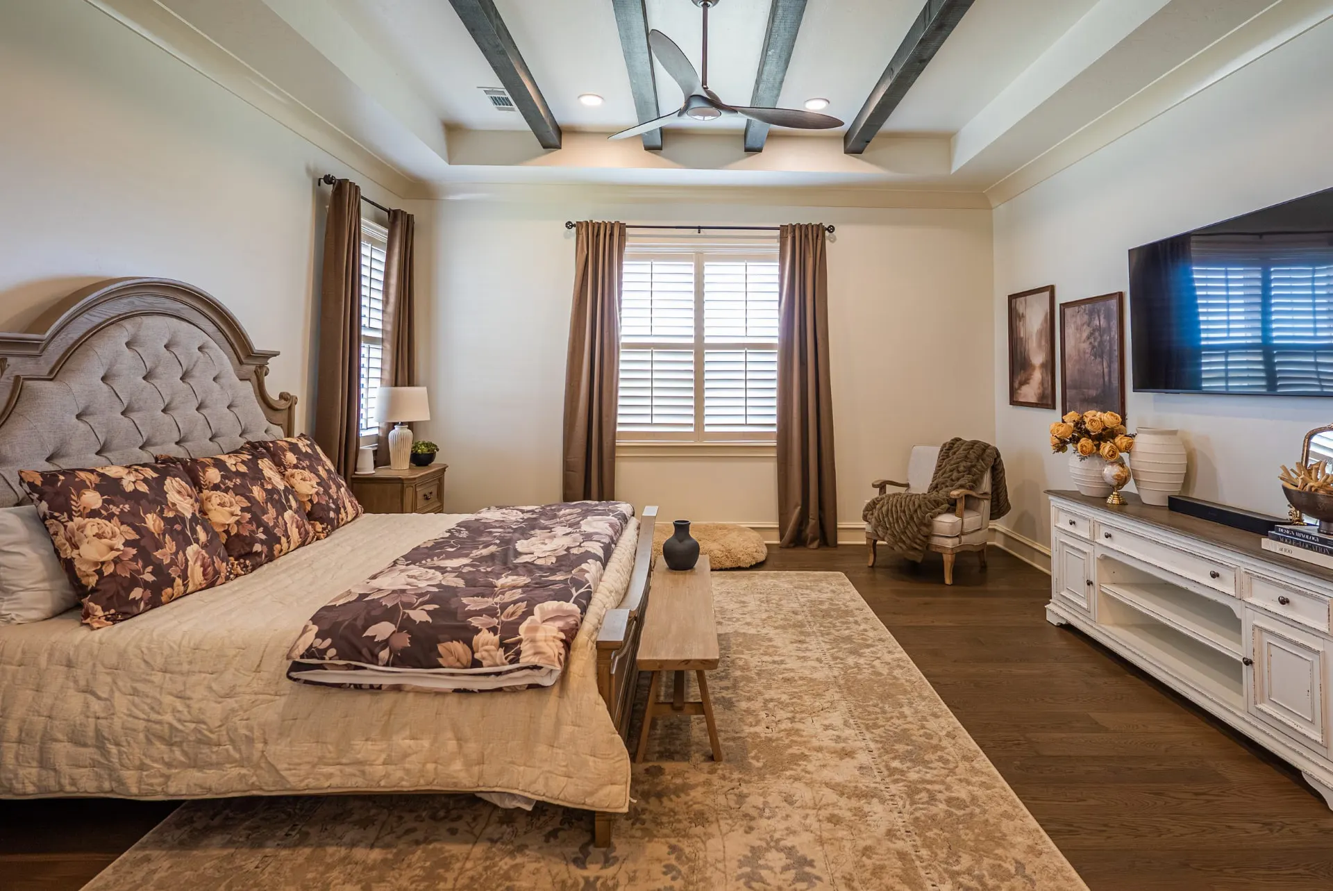 Primary bedroom at 1610 NW Eliam Dr with stained beams in a tray ceiling, tufted headboard and wide-plank wood floors