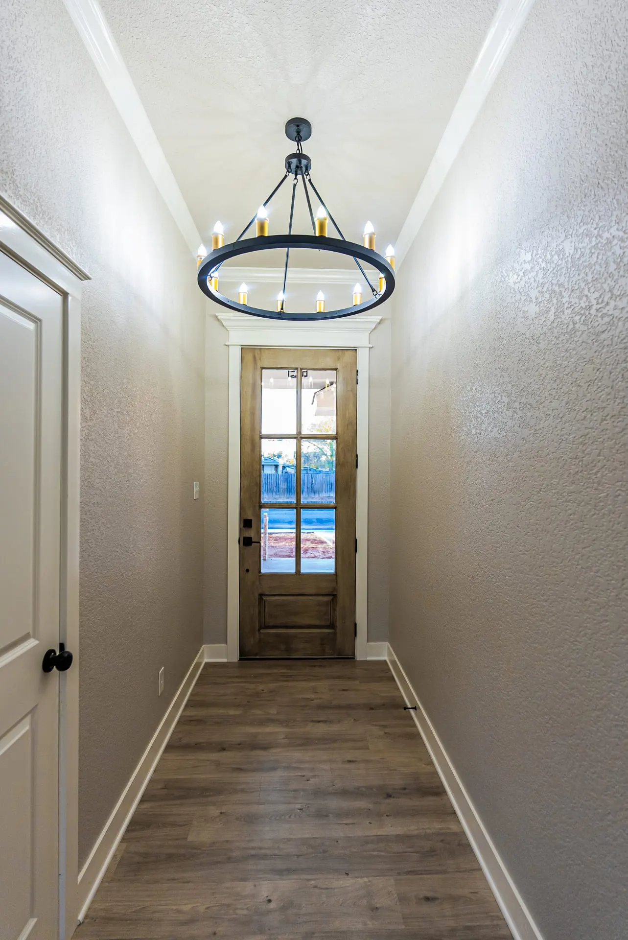 Entry hallway at 708 K Ave with a wagon-wheel chandelier, glass-paneled stained wood front door and wood-look floors