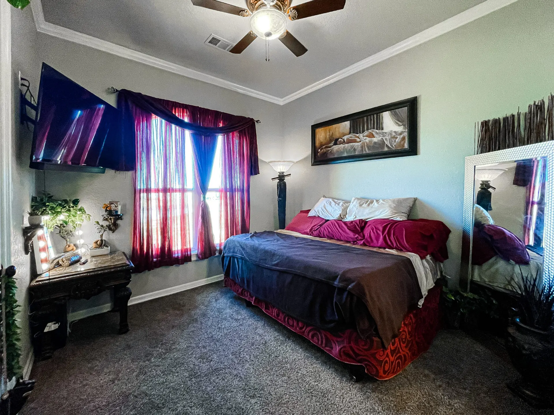 Bedroom at 8821 Shawn Dr with burgundy drapery and bedding, a wall-mounted TV, an ornate dark wood table and a wide framed floor mirror