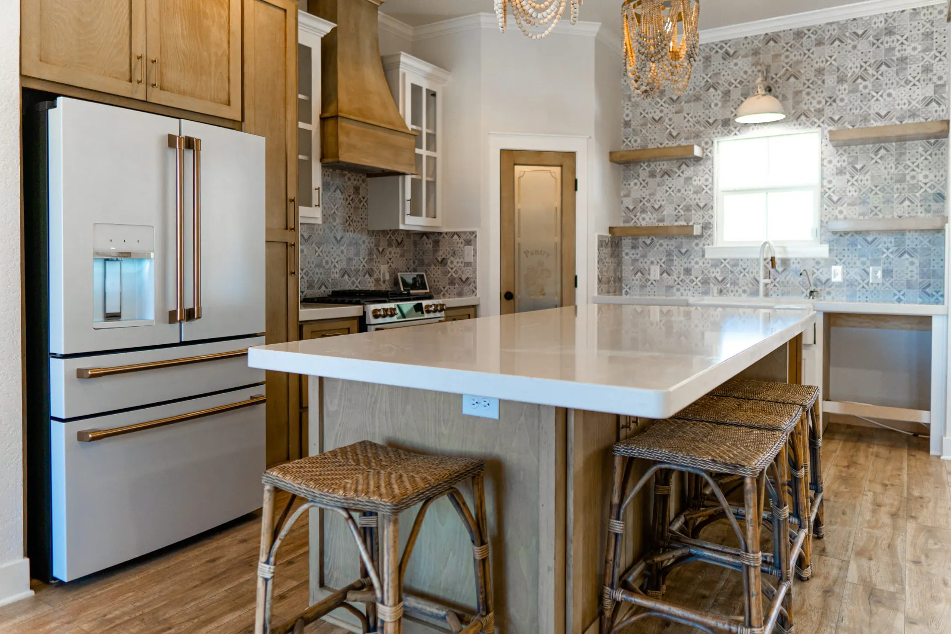 Kitchen at Sarai Home looking past the island to white glass-front cabinetry, a wood range hood and a frosted-glass pantry door
