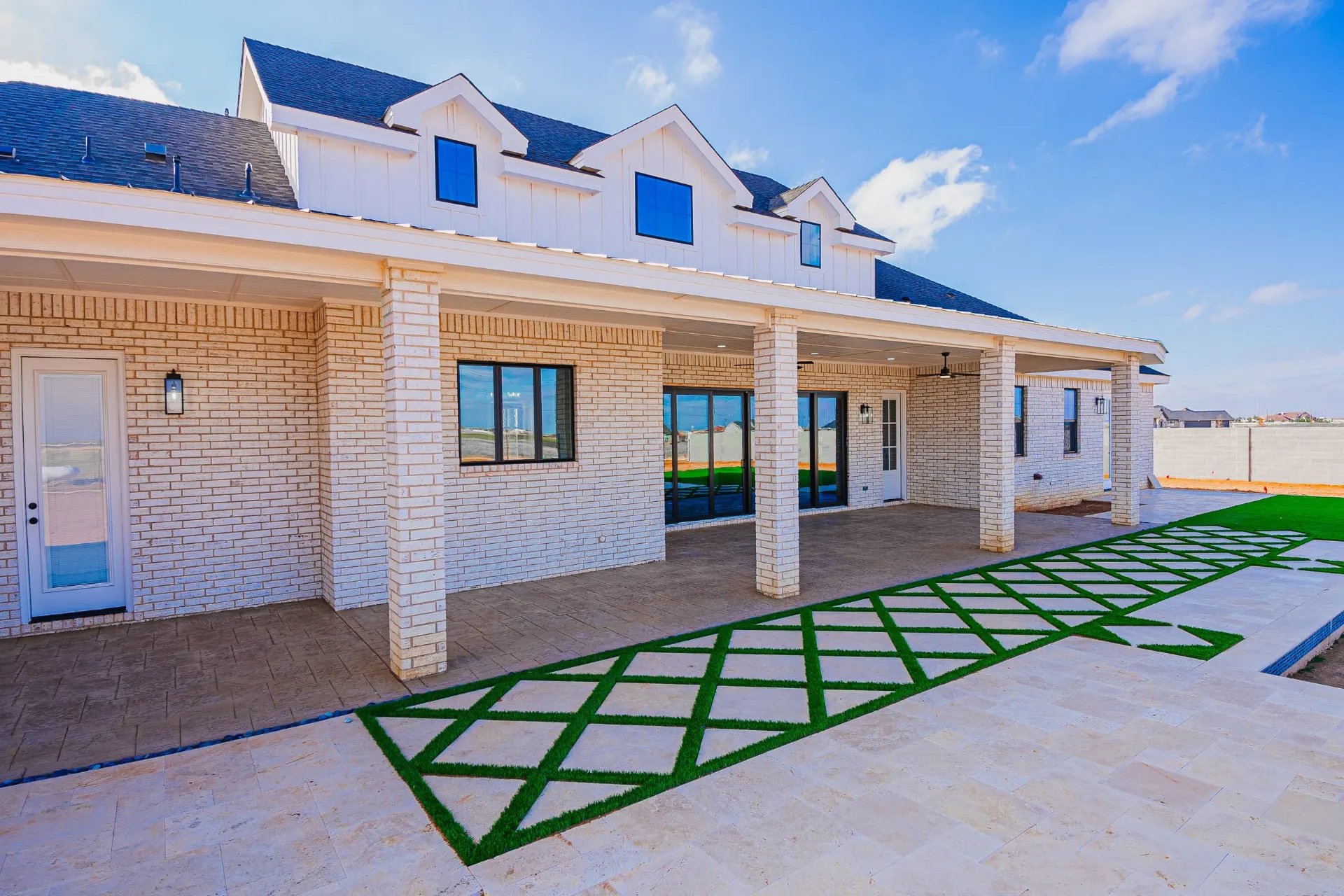 Covered back patio at 1602 NW 12th St with cream brick columns, ceiling fans and a turf-and-paver walkway