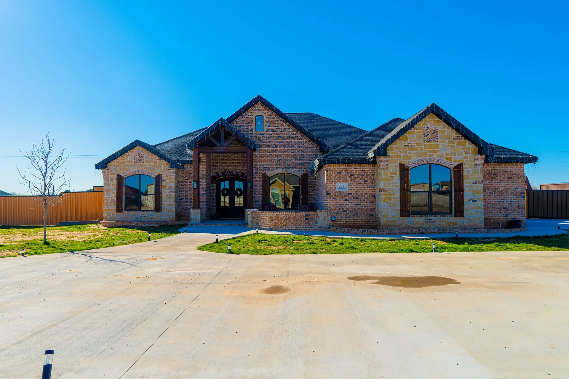Front elevation of 8821 Shawn Dr in red brick and Texas limestone with arched shuttered windows, a timber-framed entry gable and a circular drive