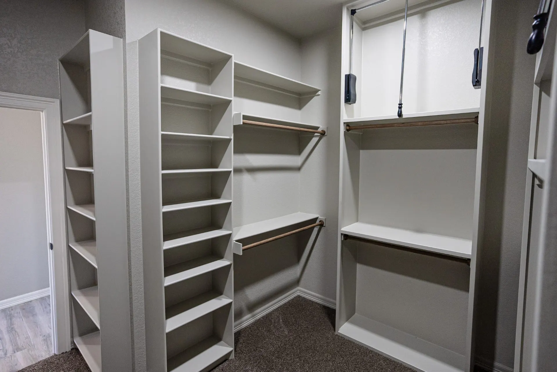 Walk-in closet at the Eliam St Home with white built-in shelving, wooden hanging rods and a shoe tower over grey carpet