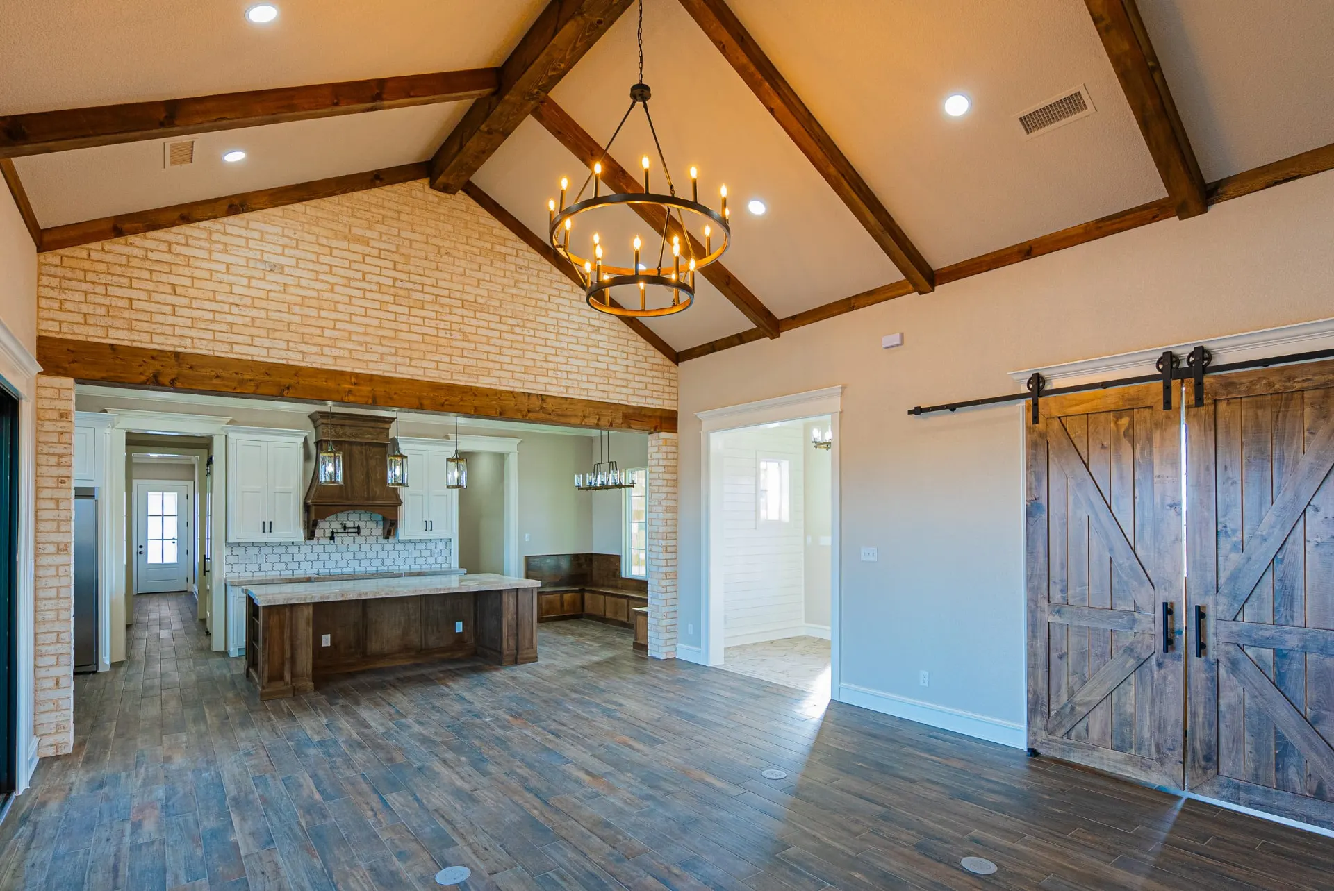 Great room at 1602 NW 12th St with whitewashed brick, vaulted timber trusses, ring chandelier and rustic barn doors to the media room
