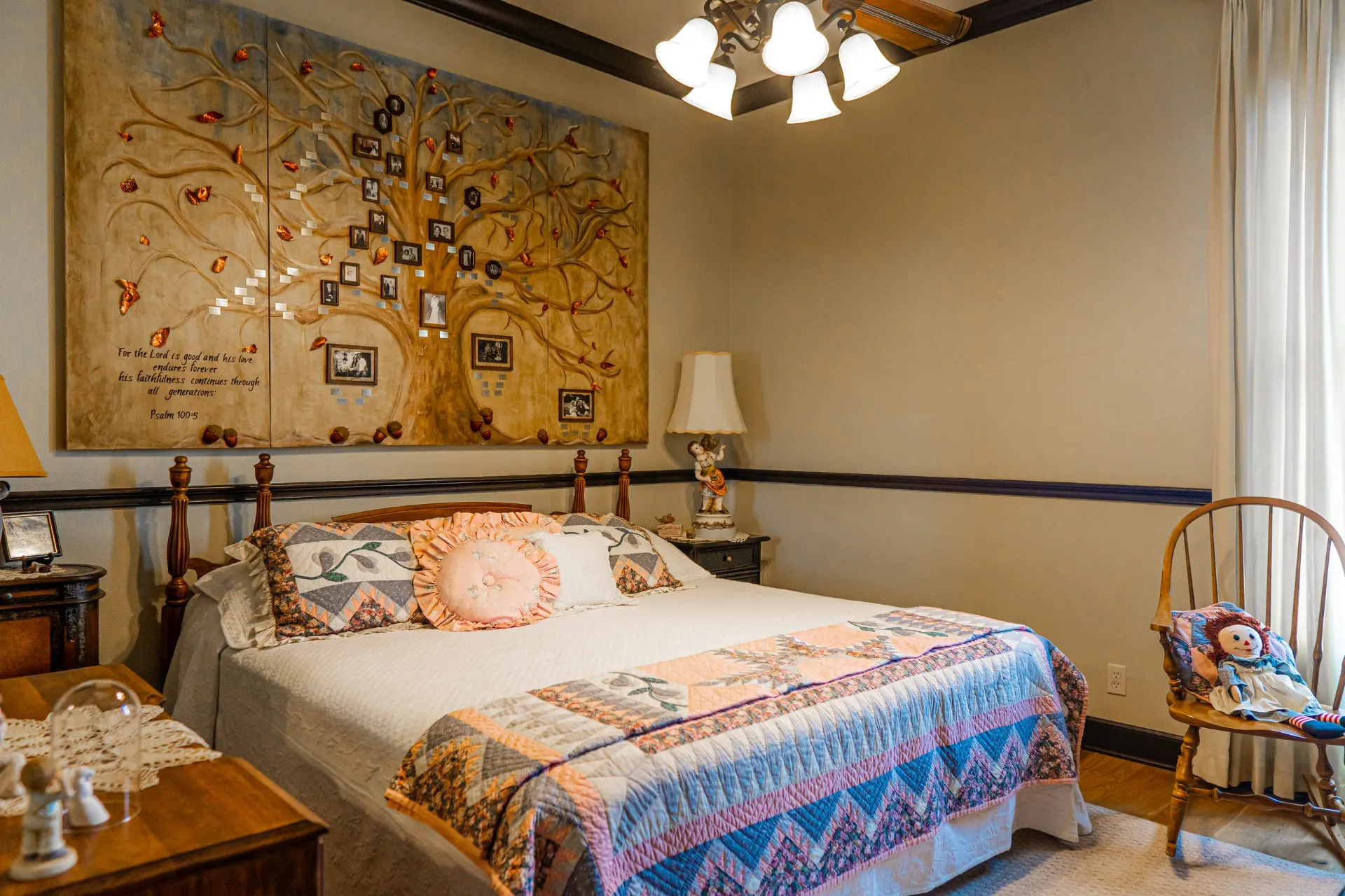 Bedroom at the Wraparound Porch Home with a four-poster bed dressed in quilts beneath a hand-painted family-tree mural bearing the words of Psalm 100:5