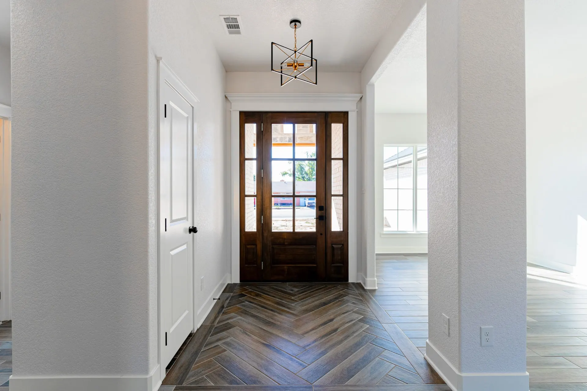 Foyer at 718 K Ave with herringbone wood-look tile, a dark wood front door with glass lights and sidelights, and a black-and-gold geometric pendant