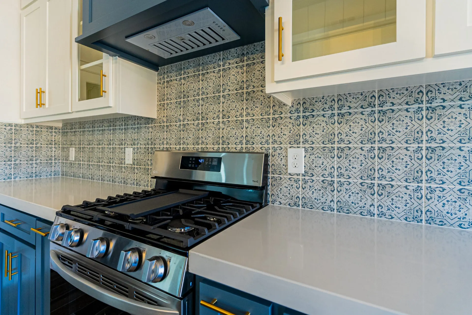 Gas range at 718 K Ave beneath a teal hood with hand-painted-look blue patterned tile backsplash