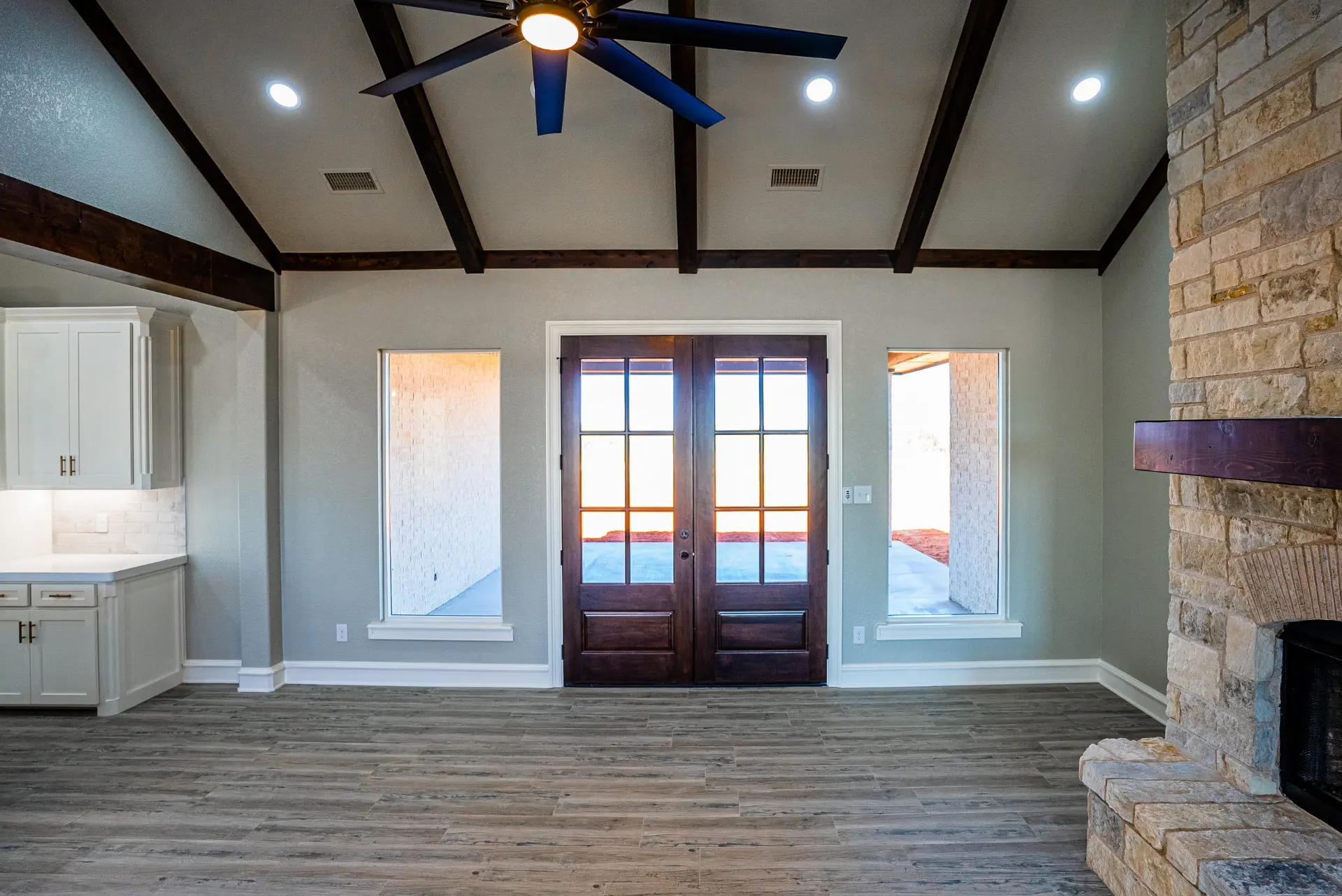 Living room at the Eliam St Home facing the rear double doors between twin windows, beside a full-height stone fireplace with a dark wood mantel