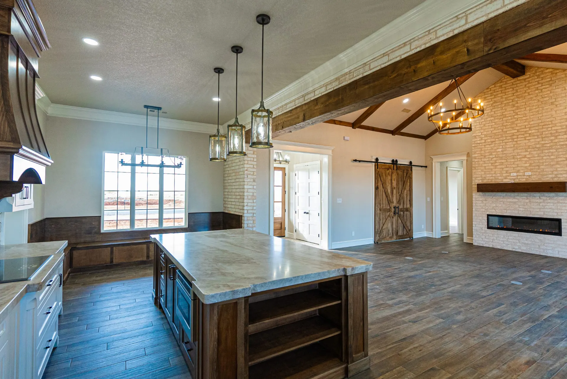 Kitchen and great room at 1602 NW 12th St with a large island, cream marble counters, stained wood hood and whitewashed brick fireplace