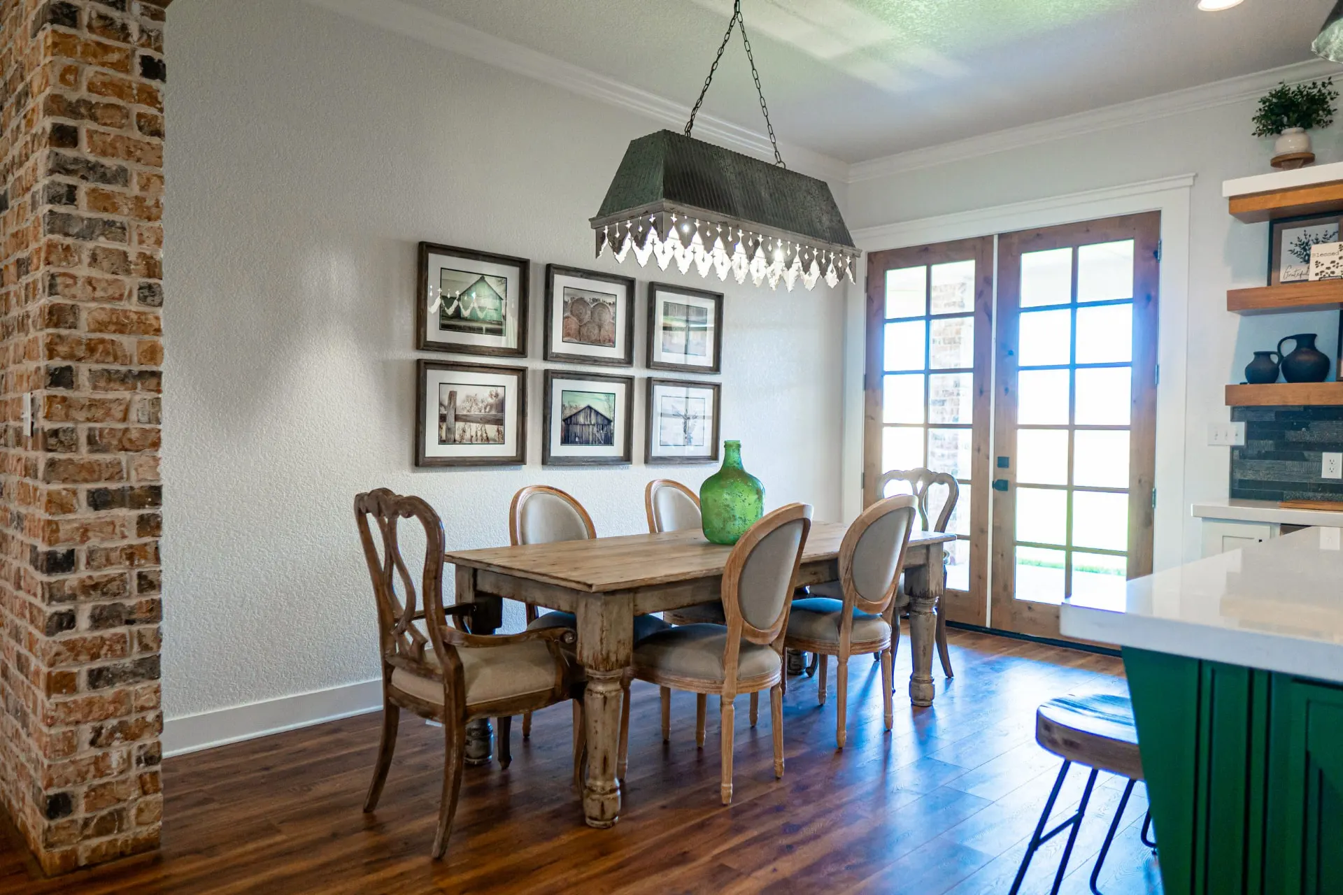 Dining area at the K Ave Farmhouse with a rustic wood table, oval-back cane chairs, a corrugated metal chandelier, a green glass jug and a gallery wall of barn prints