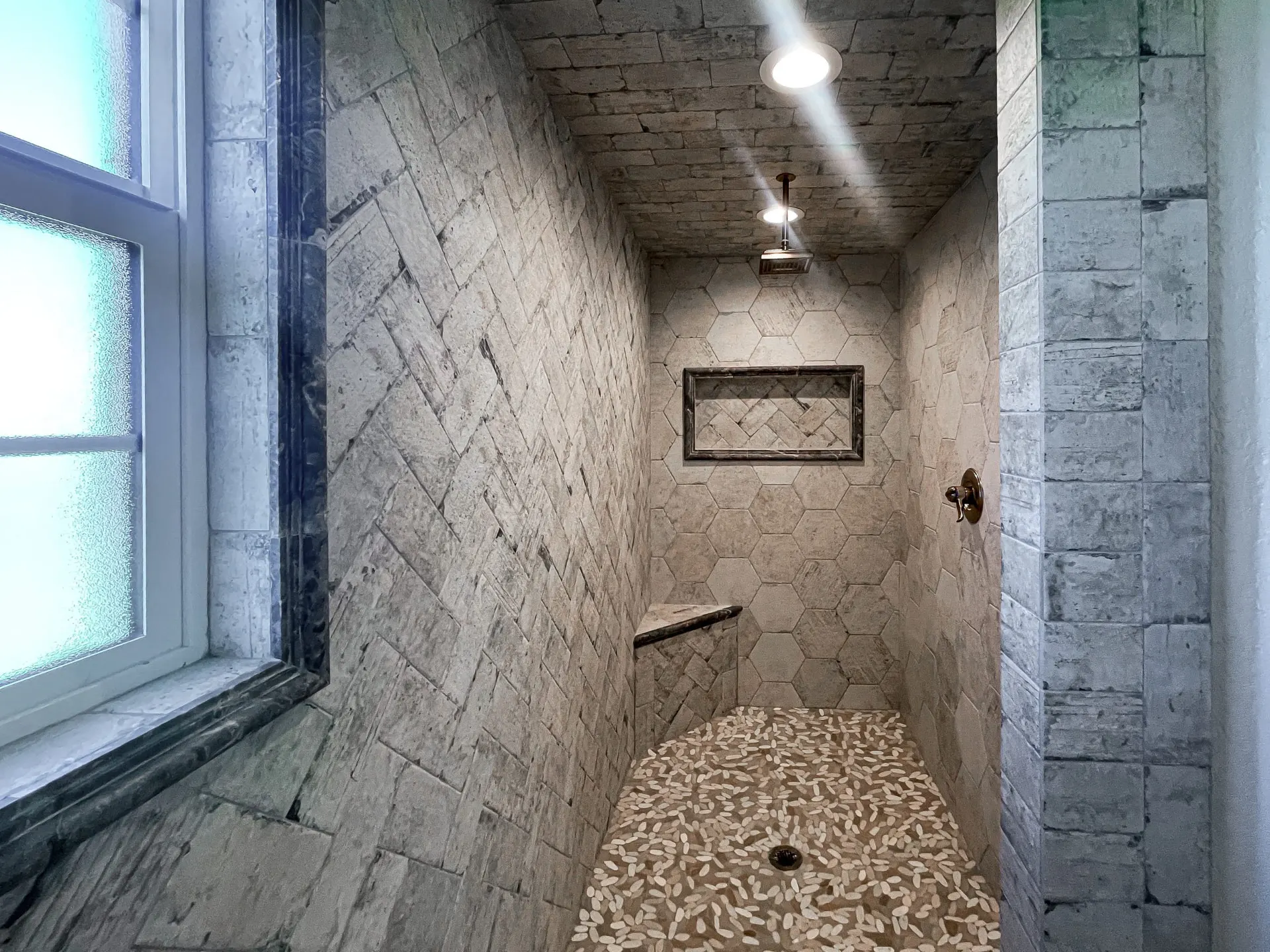 Walk-in shower at 1615 NW 12th St with herringbone stone tile, hexagon inset niche, pebble floor and stained-wood-look ceiling tile