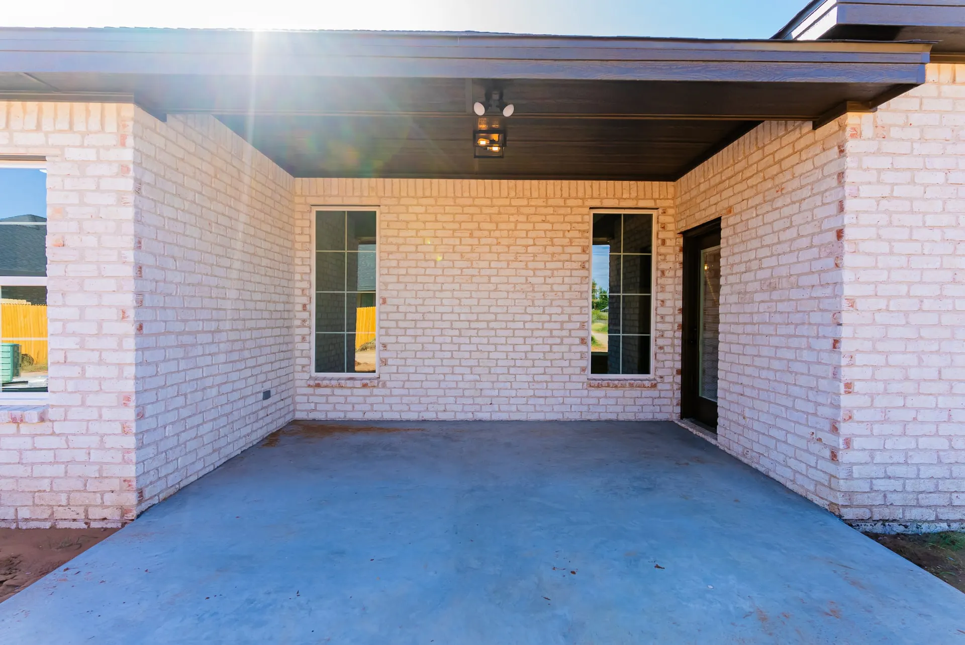 Covered patio at 718 K Ave in whitewashed brick with a dark paneled ceiling, grid windows and a concrete slab
