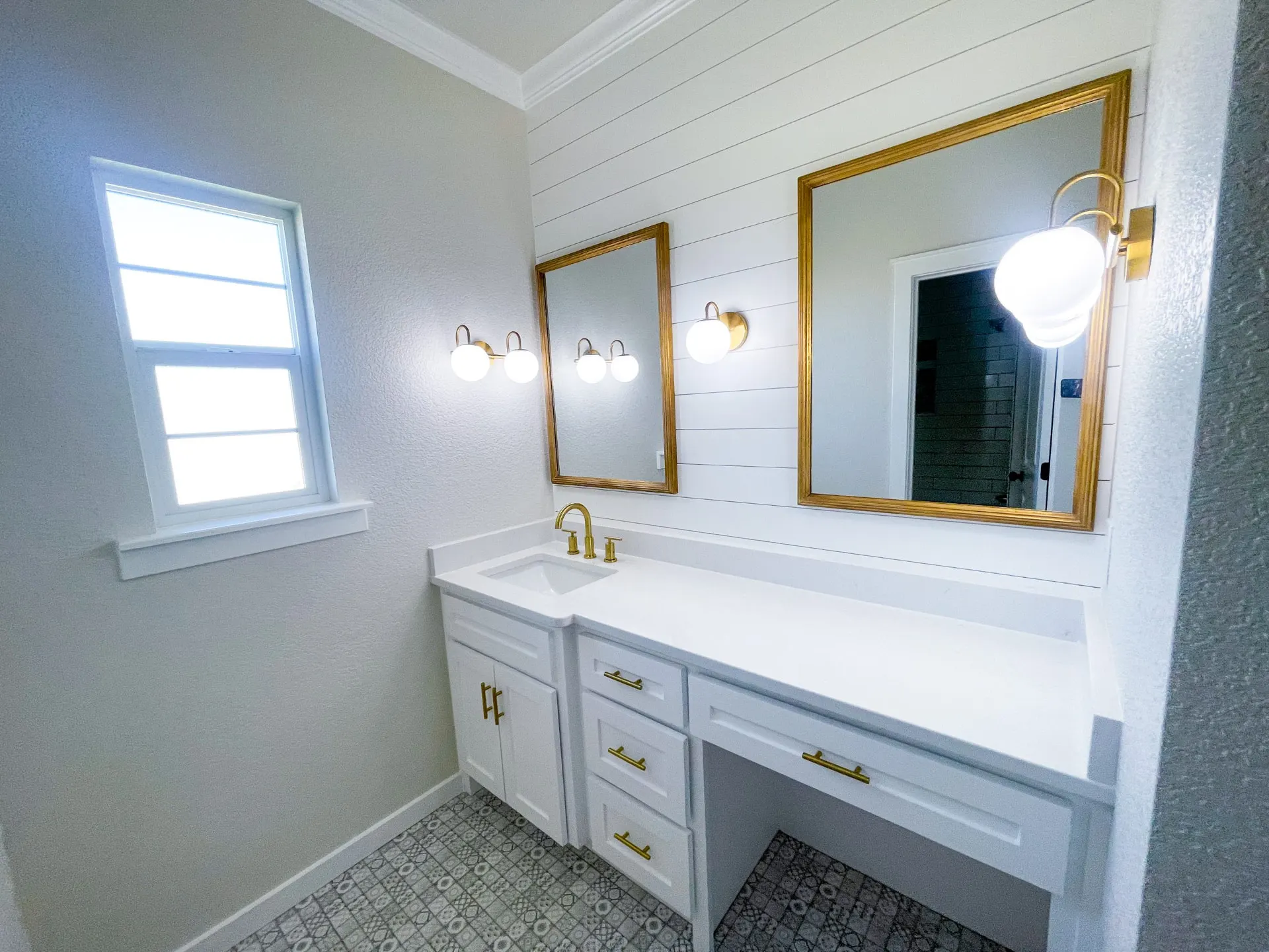 Bathroom vanity at 1615 NW 12th St with white shiplap wall, gold-framed mirrors, glass globe sconces and patterned tile floor