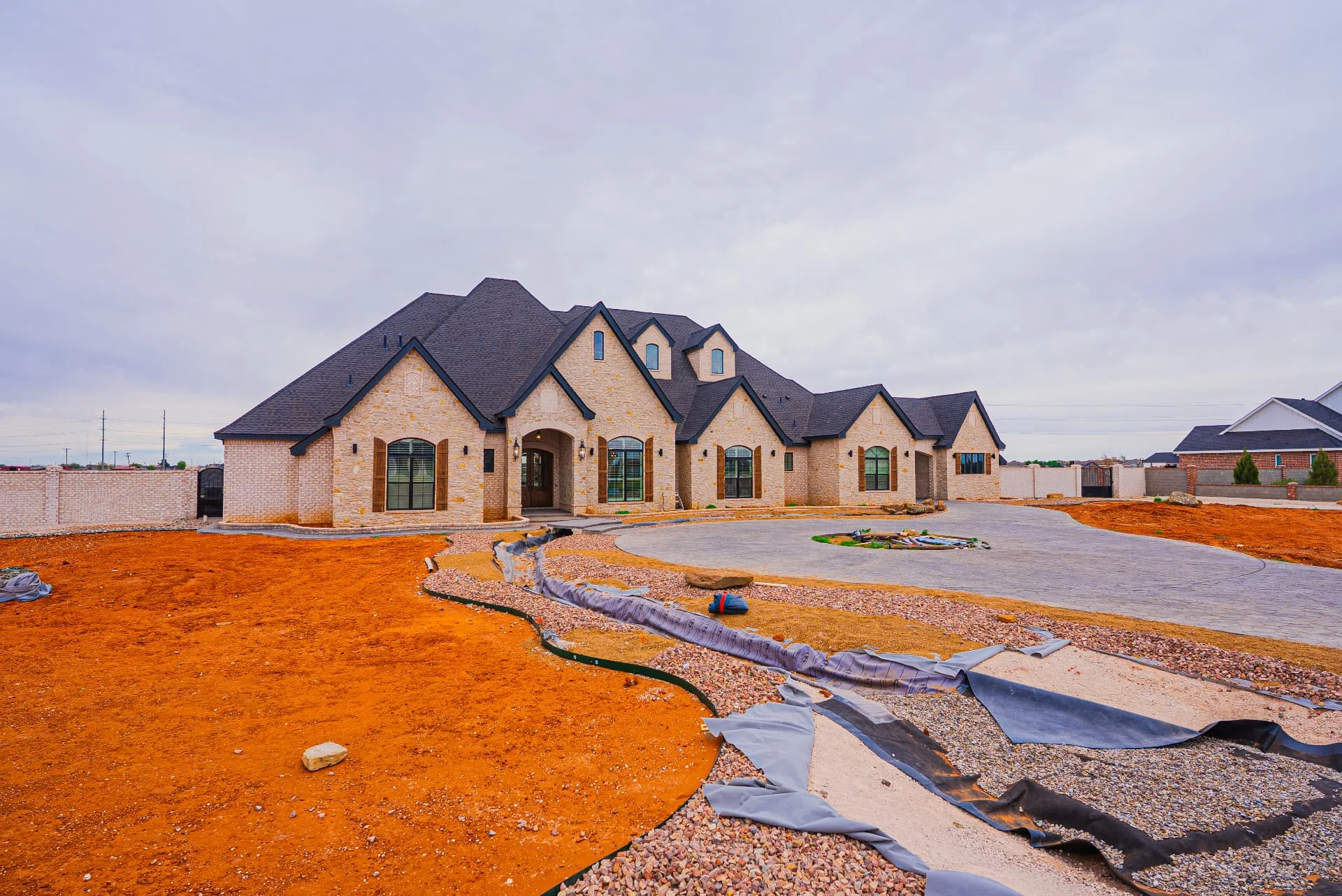 Front exterior of The Flores Estate with stone facade and circular driveway during landscaping