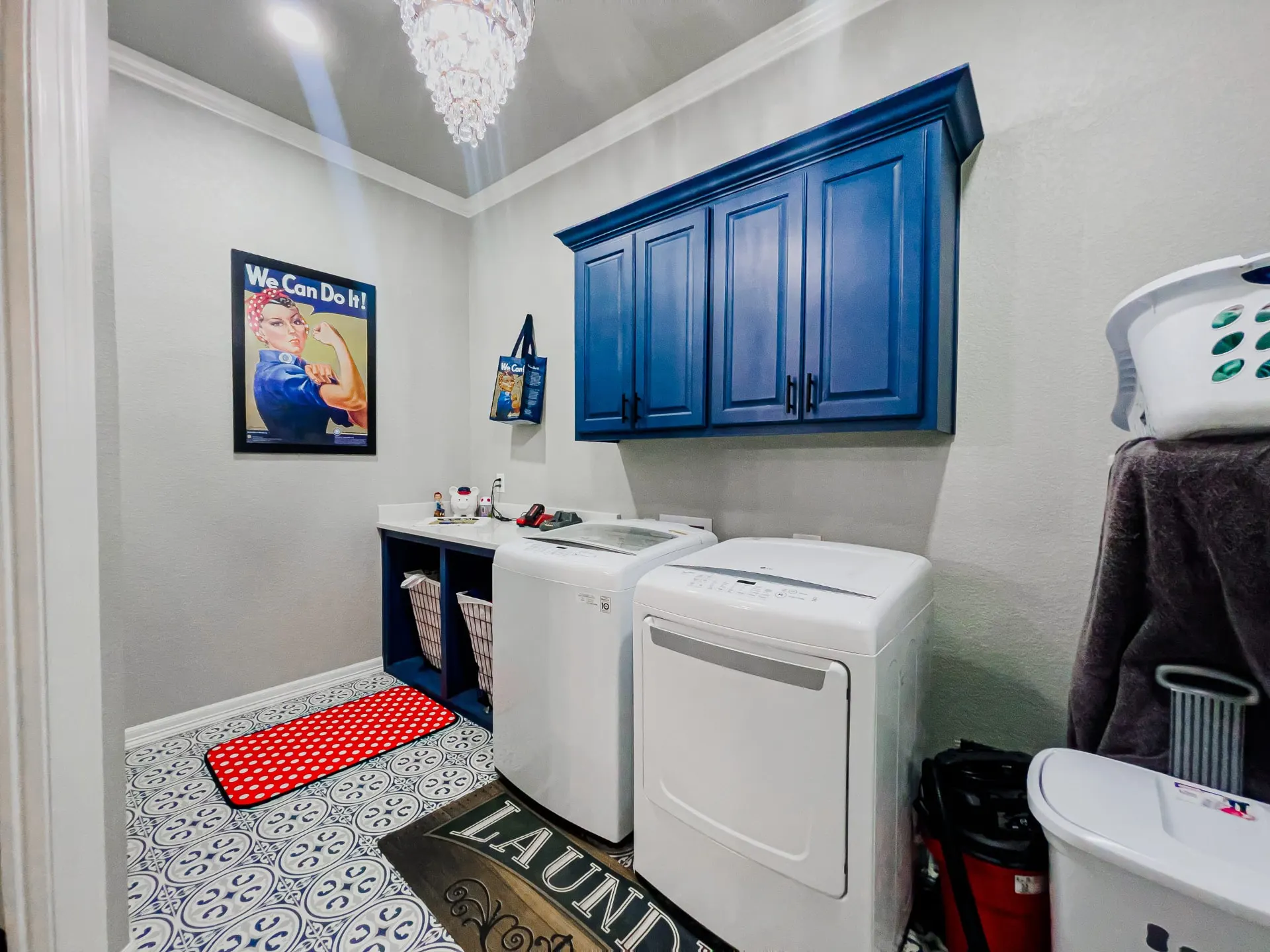 Laundry room at 8821 Shawn Dr with navy wall cabinets, a white folding counter over hamper cubbies, a white washer and dryer and blue patterned floor tile