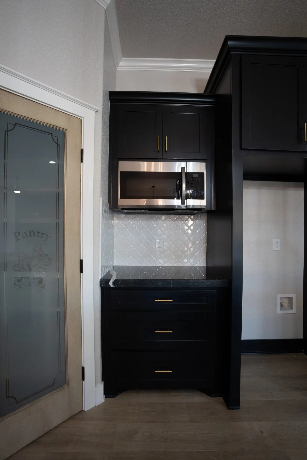 Coffee and microwave station at 708 K Ave with black cabinetry, brass pulls, arabesque tile backsplash and the etched-glass pantry door beside it