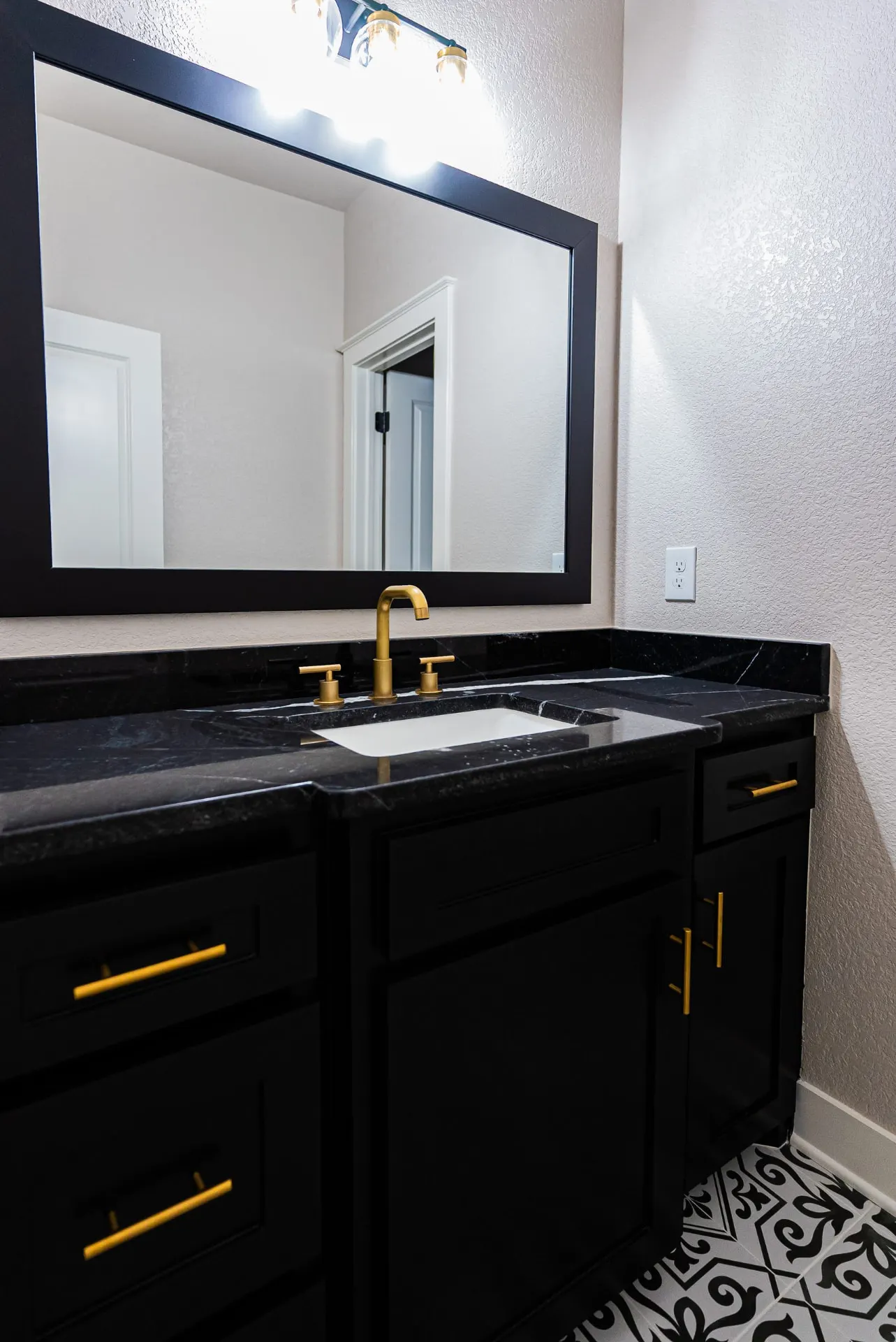 Bathroom vanity at 708 K Ave with black cabinetry, black marble counter, brushed gold faucet and hardware and black-and-white patterned floor tile
