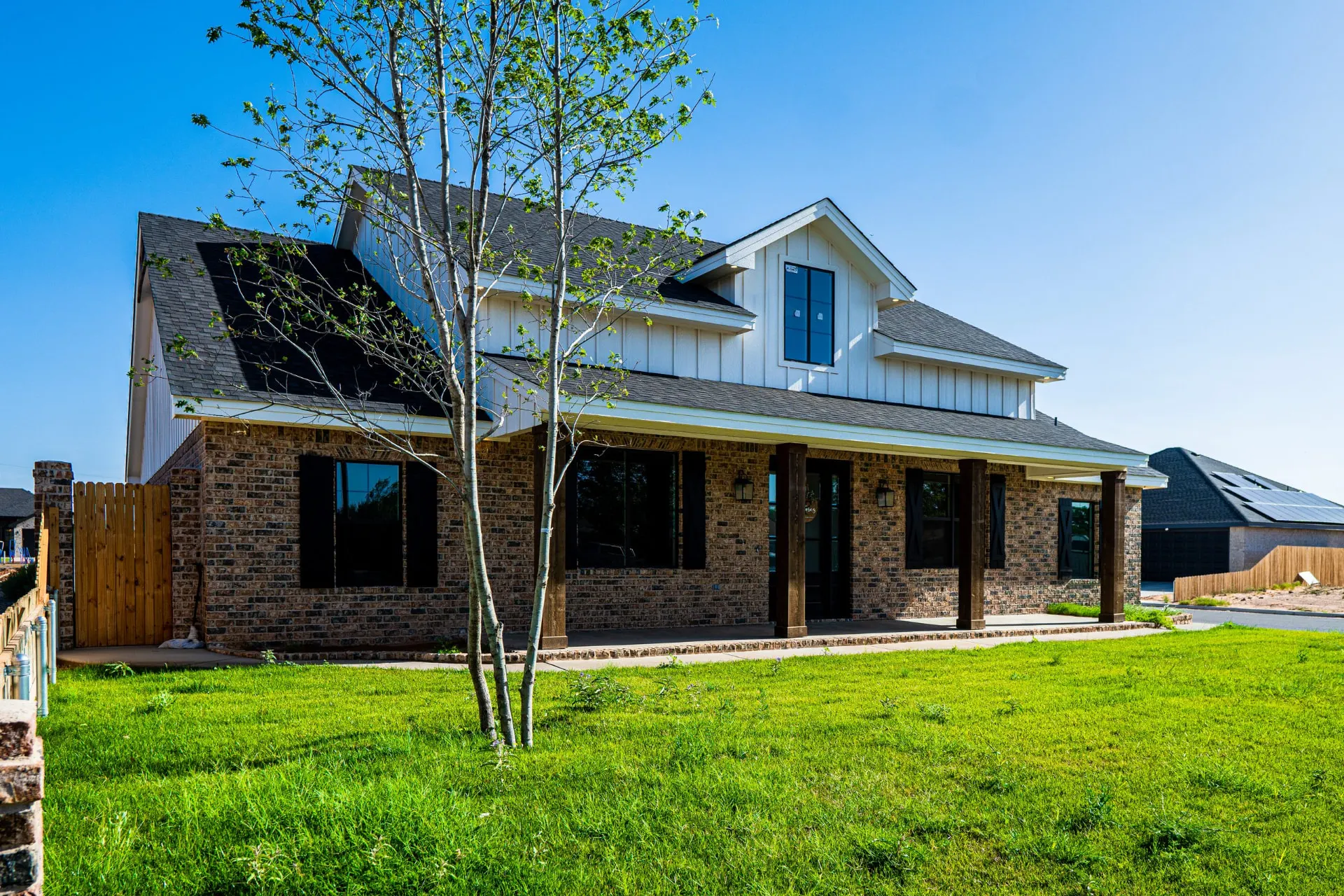 Front view of the K Ave Farmhouse with a young tree in the lawn, timber porch columns and black window shutters