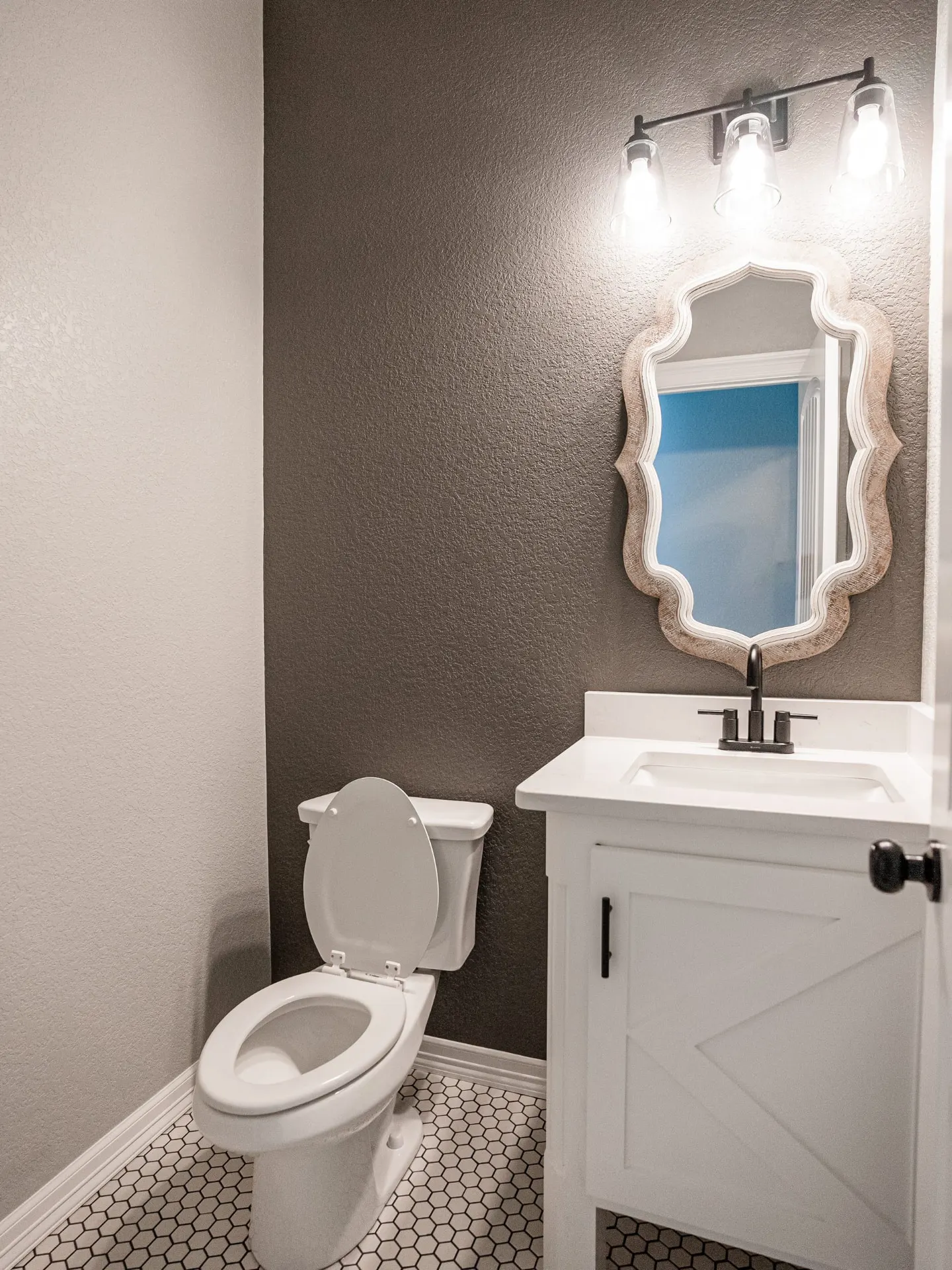 Powder room at the Eliam St Home with a white barn-door vanity, black faucet, quatrefoil-edge mirror, brown-grey feature wall and black-and-white hexagon floor