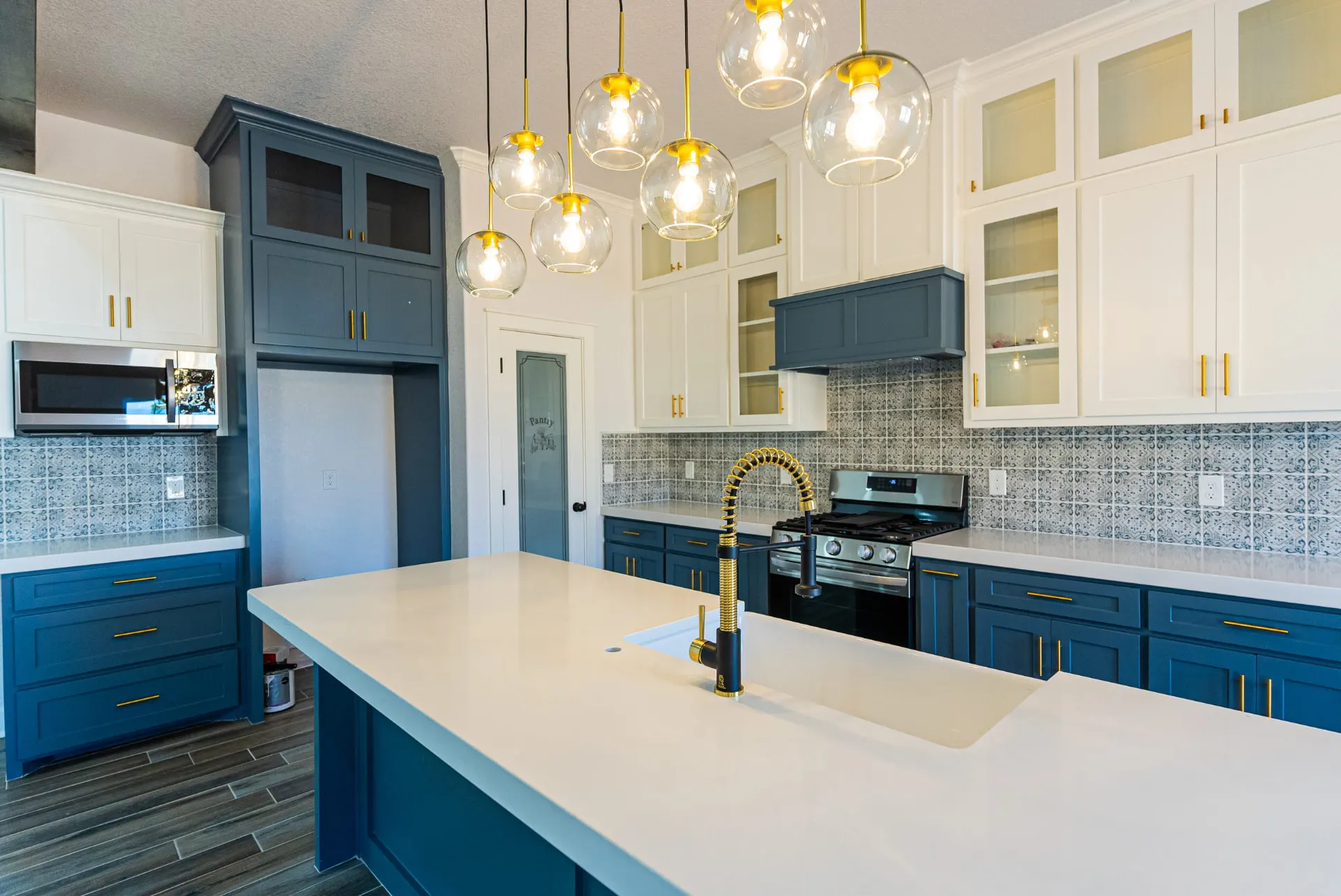 Island view at 718 K Ave with a white farmhouse sink, black-and-gold coil faucet and gold hardware on teal and white cabinetry