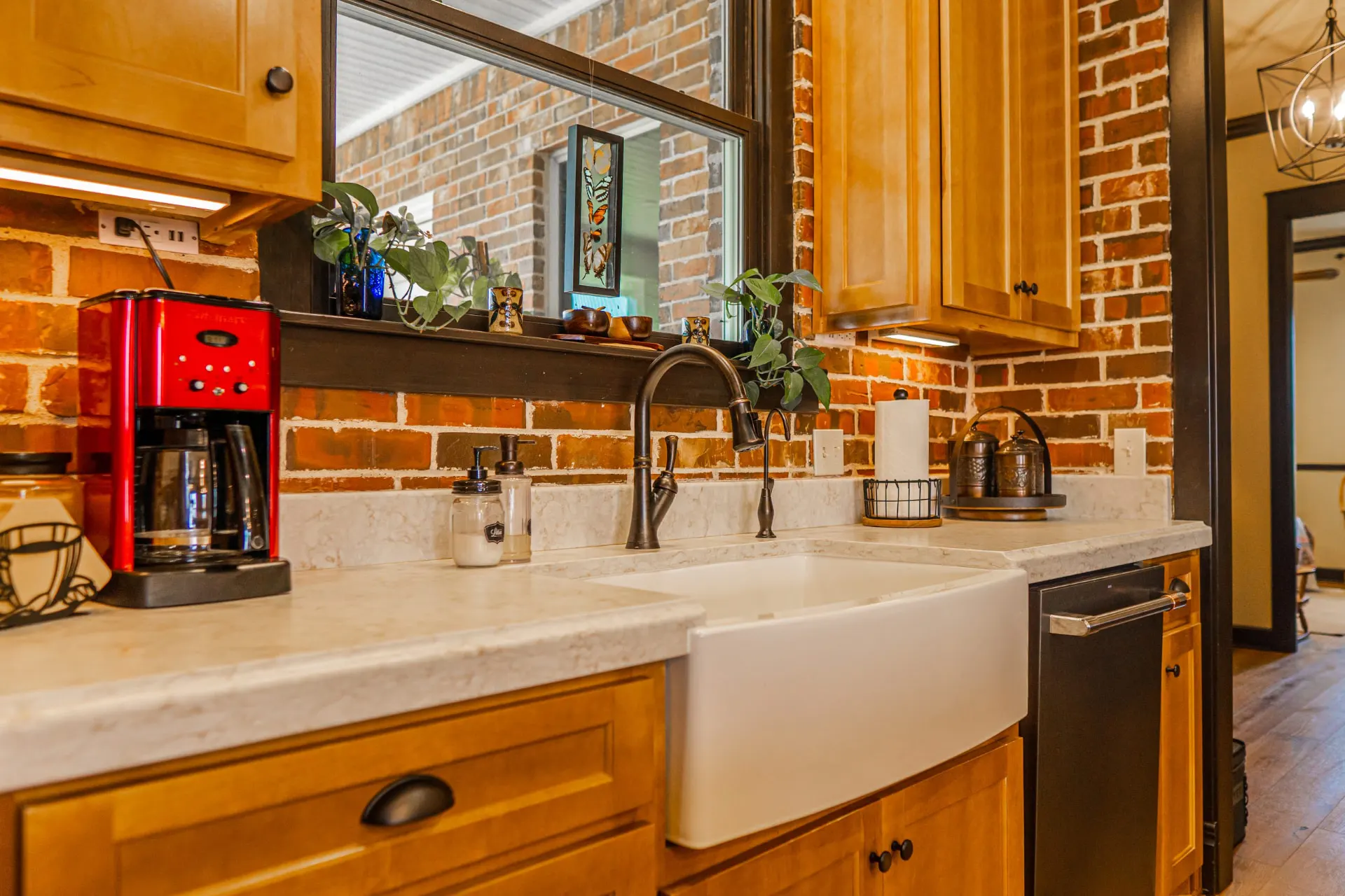 Kitchen sink wall at the Wraparound Porch Home with a white farmhouse sink, bronze faucet, honey-oak cabinetry and a red brick backsplash under an interior window