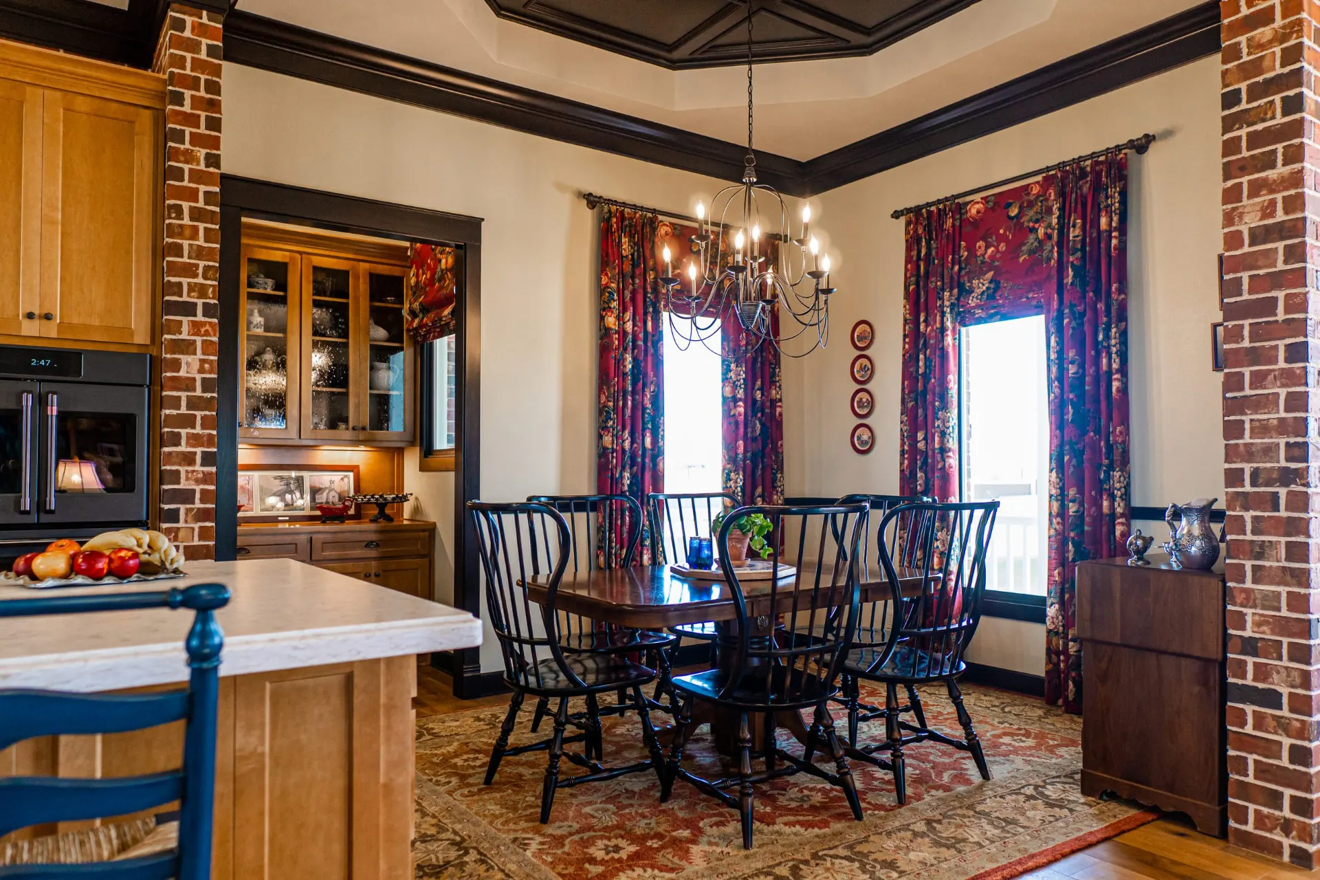 Dining room at the Wraparound Porch Home with a dark coffered tray ceiling, iron candle chandelier, Windsor chairs and brick pillars