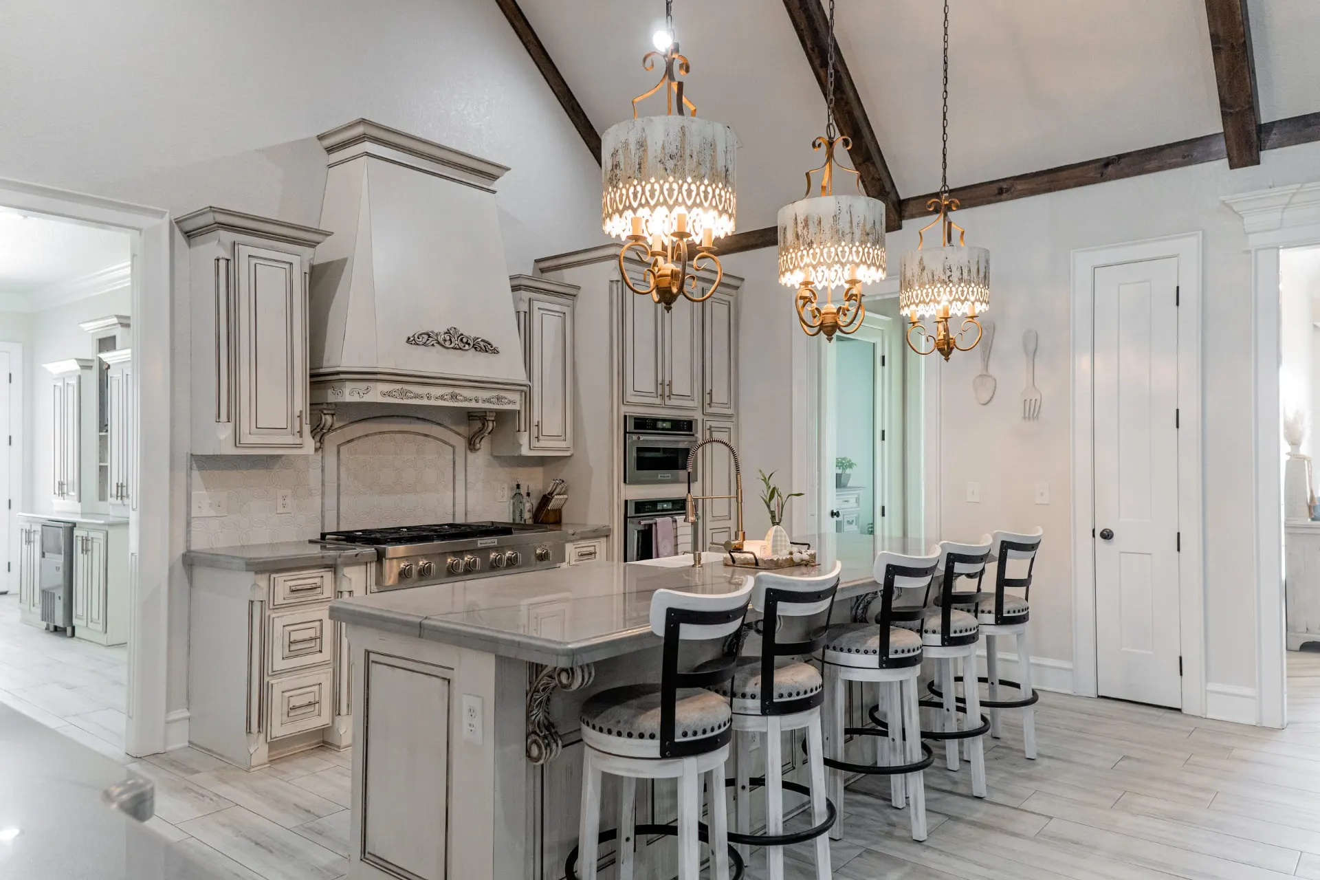 Kitchen island at 1667 Eldenrod with distressed white cabinetry, filigree chandeliers and a carved decorative hood