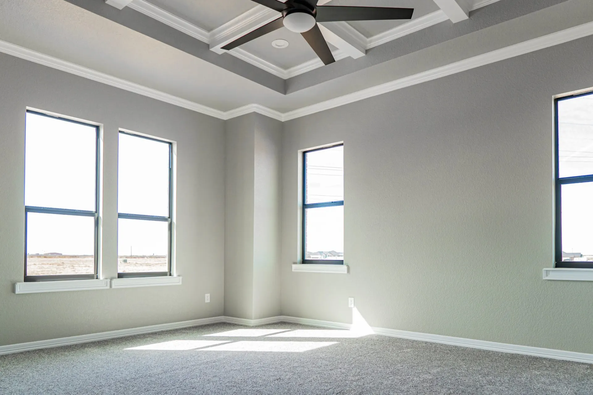 Primary bedroom at the 12th St Home with a coffered tray ceiling, dark fan and corner windows