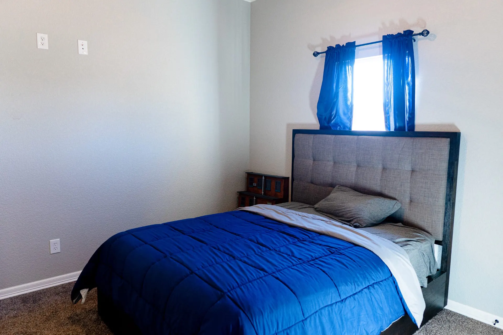 Bedroom at 8821 Shawn Dr with a gray tufted headboard, blue bedding and sheer curtains over a bright window