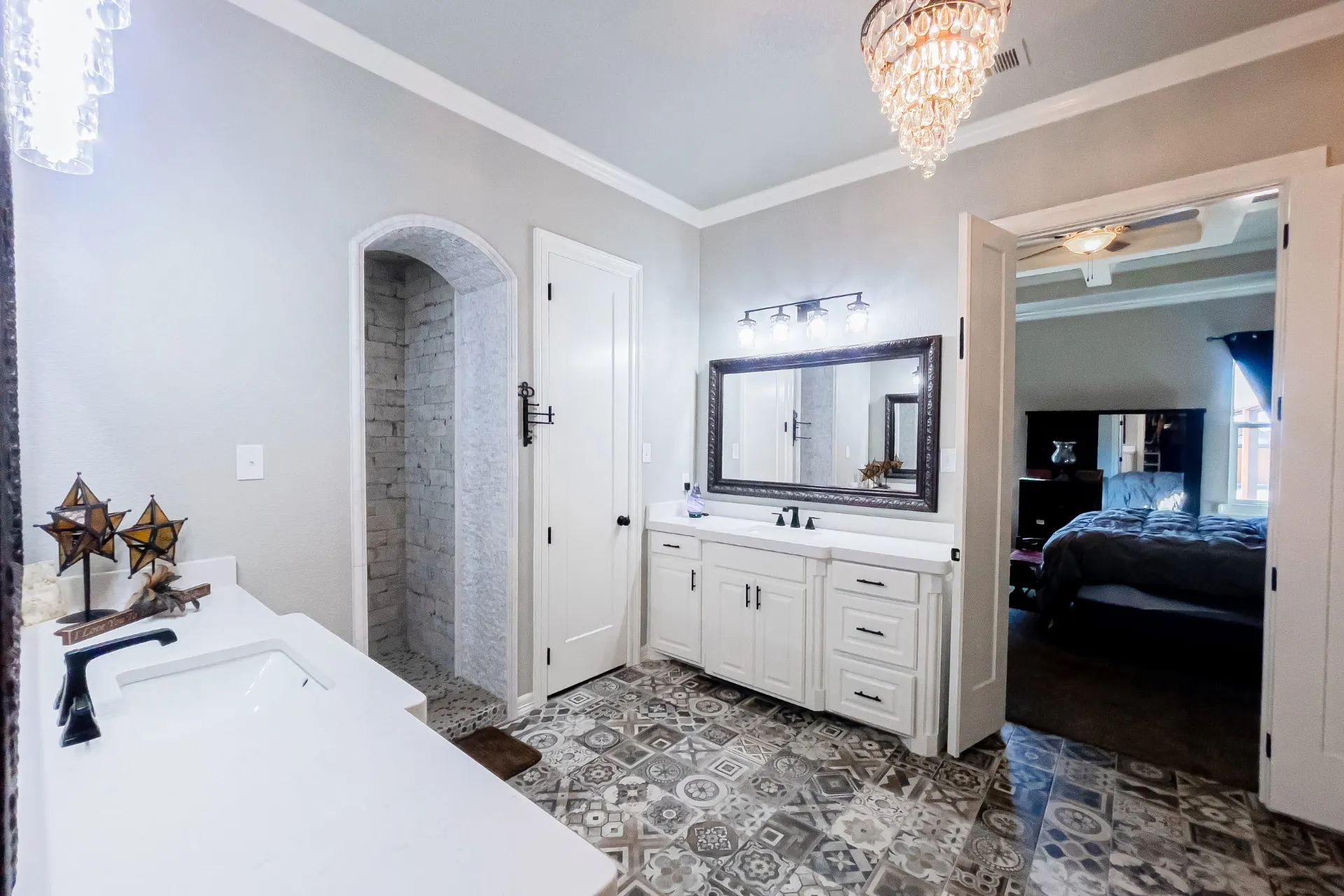 Primary bath at 8821 Shawn Dr with white shaker vanities, matte black faucets, a large dark-framed mirror, a cascading crystal chandelier and an arched curbless walk-in shower
